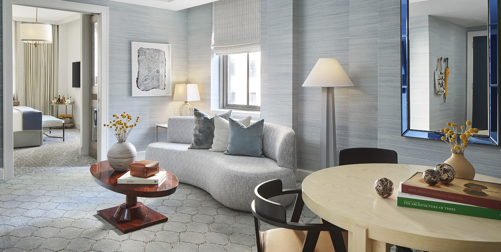 A wide view of a hotel suite's living area with a sofa, coffee table, dining table, and lamp.