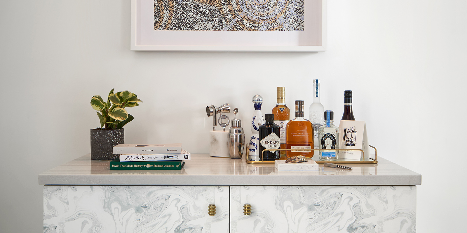 A marble cabinet with liquor bottles, bar tools, and books on top