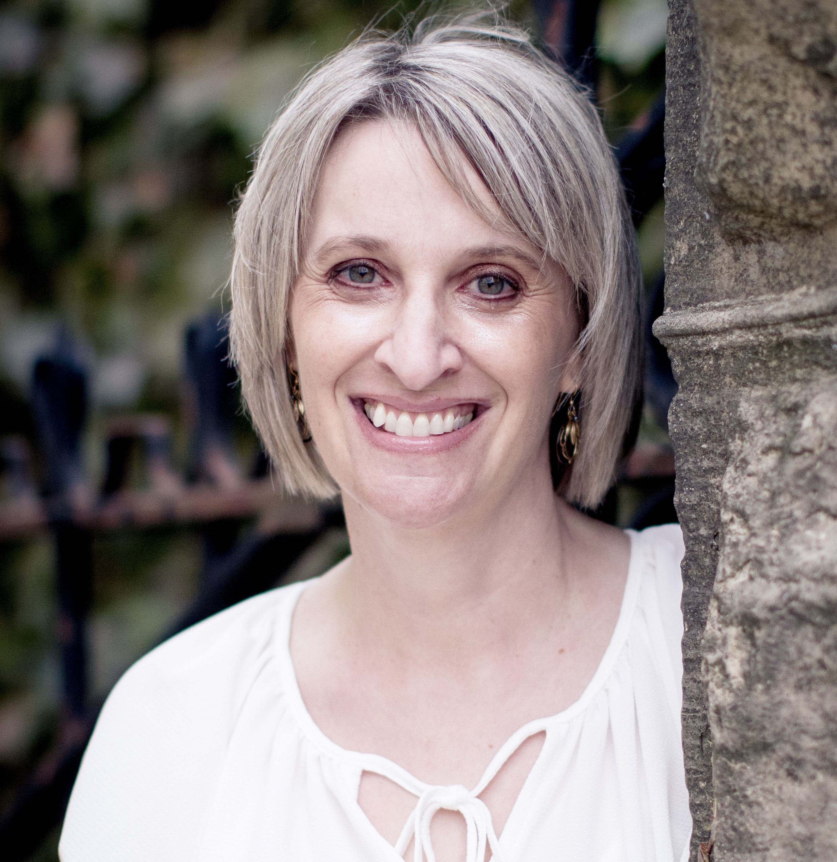 Alice, a woman with short blonde hair and light eyes wearing a white blouse. 