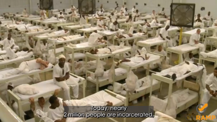 A full room in a prison with bunk beds and incarcerated individuals in white jumpsuits. 