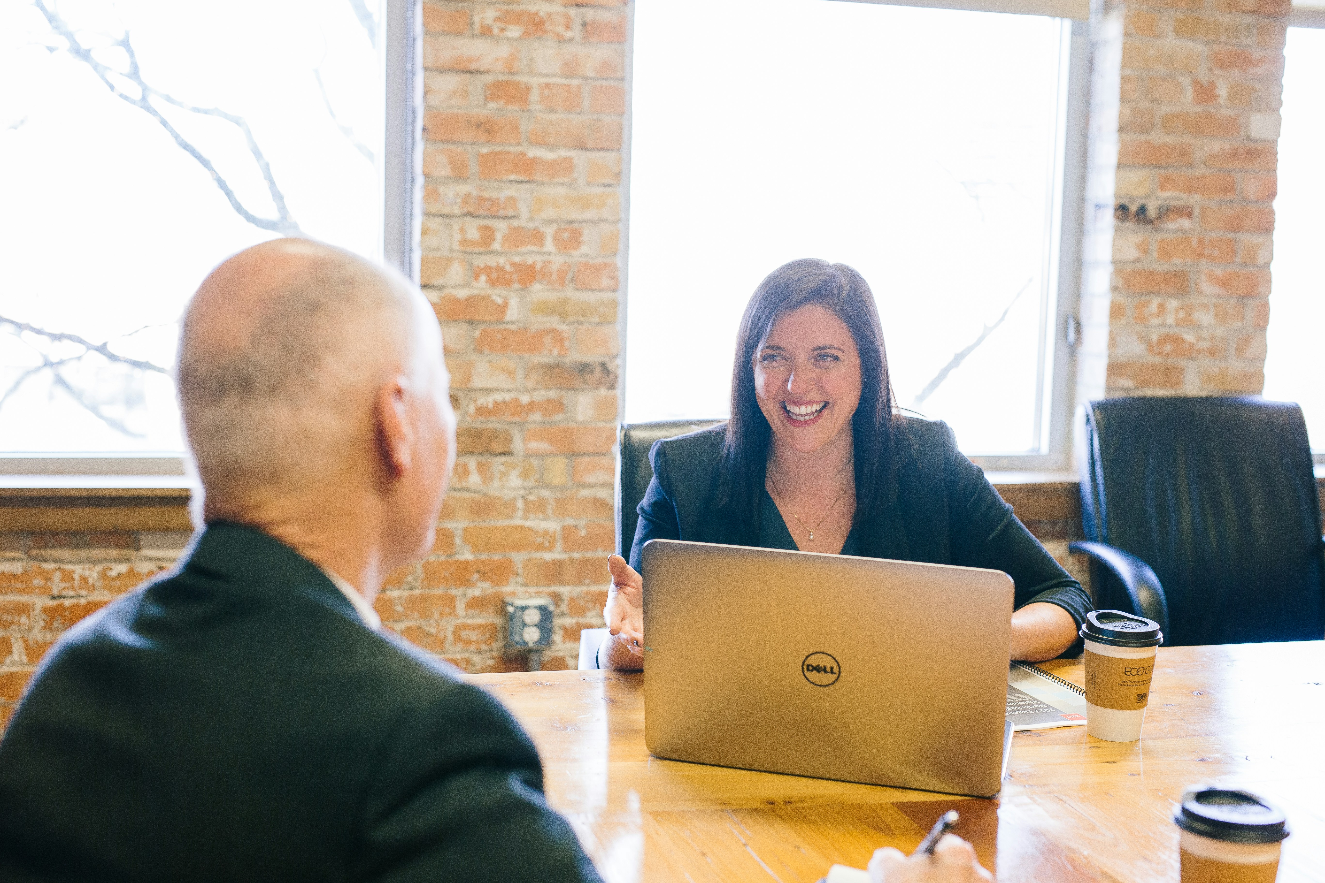 Man and woman sitting across a desk from each other, with the woman smiling, illustrating a supportive mentoring conversation.