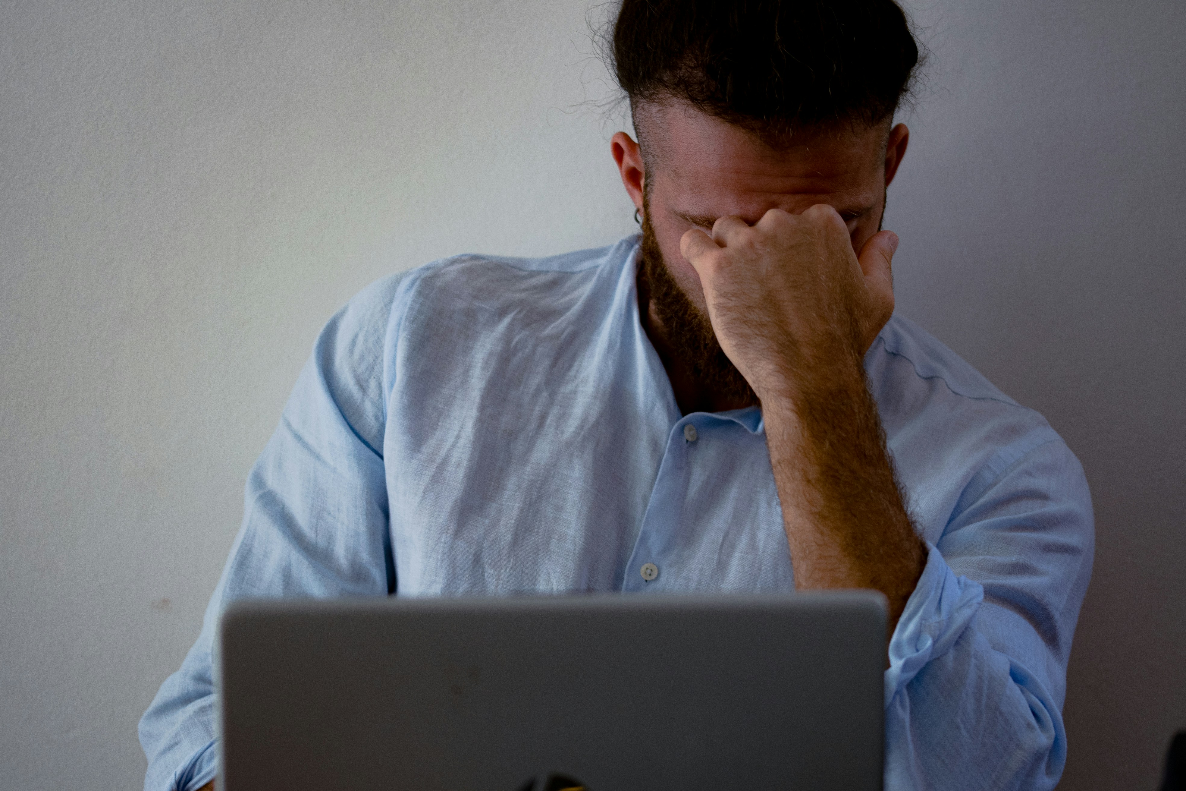 A man sitting at his desk with his head in his hands, looking frustrated and stressed. Papers and a laptop are in front of him, conveying tension and difficulty in a work environment. Used to illustrate challenges in navigating conflict.