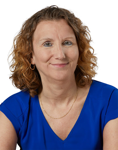 Woman with curly blond hair, shoulder length, wearing a bright blue shirt, smiling into the camera