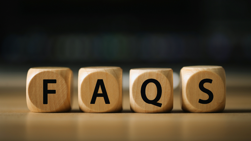 Blurred background. Four wooden dice sit on a table and spell out the word FAQS.