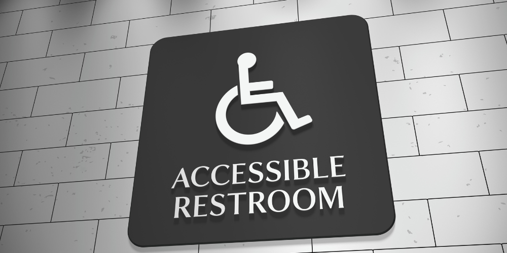 Black and white Accessible Restroom signage affixed to a white tile wall.