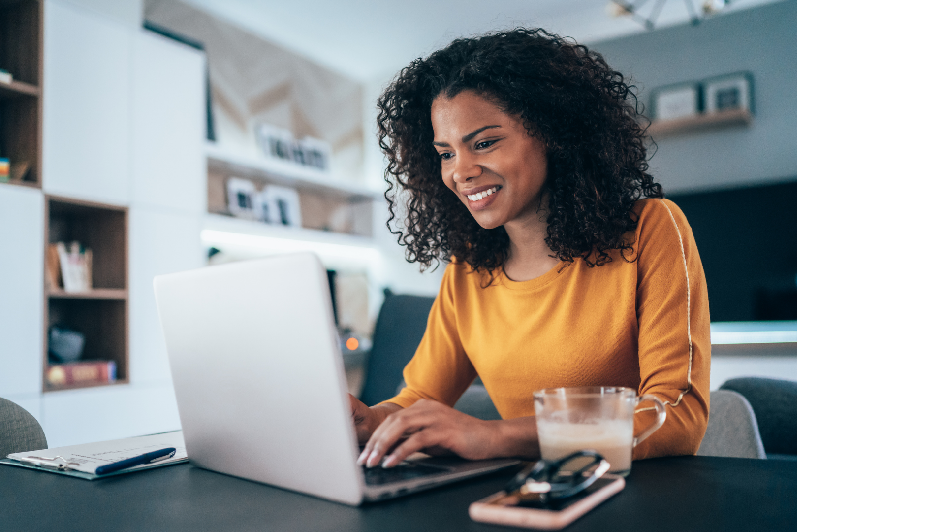 a woman in a room with pictures hanging on shelves working at her laptop and smiling
