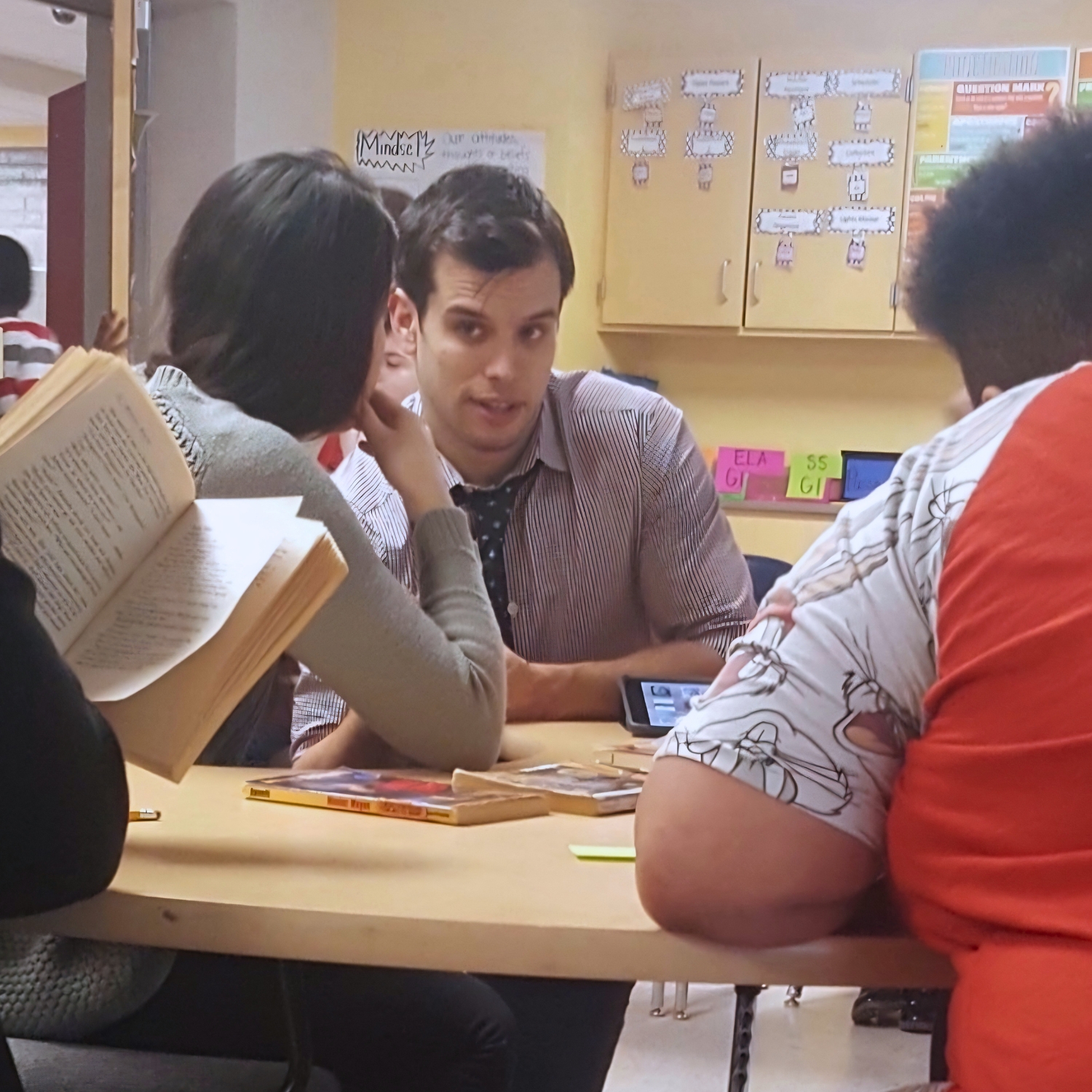 Gerrit sits with students around a classroom table as they practice a daily fluency routine with open books.