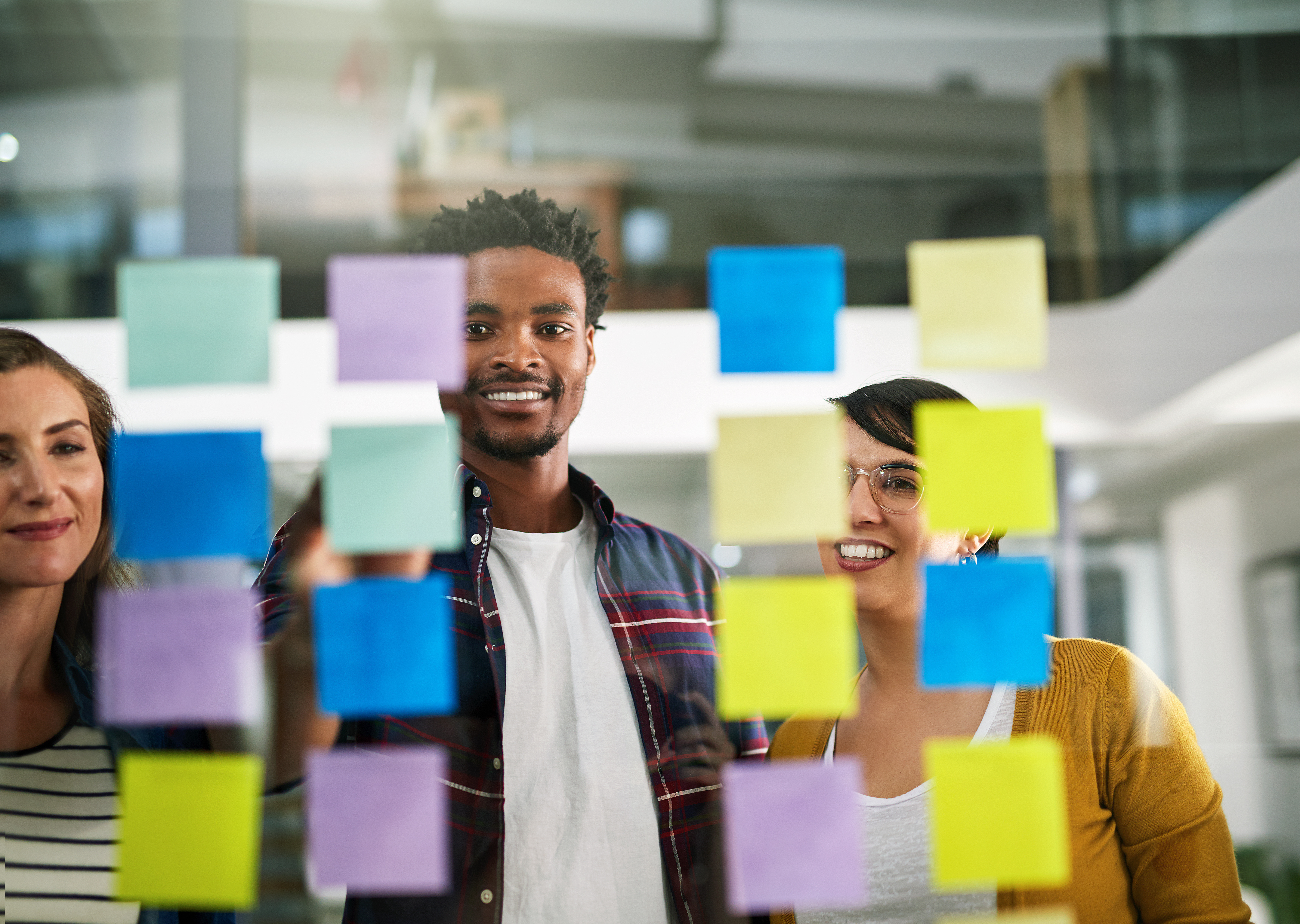 Three people facing a board smiling while placing post it notes on the board. 