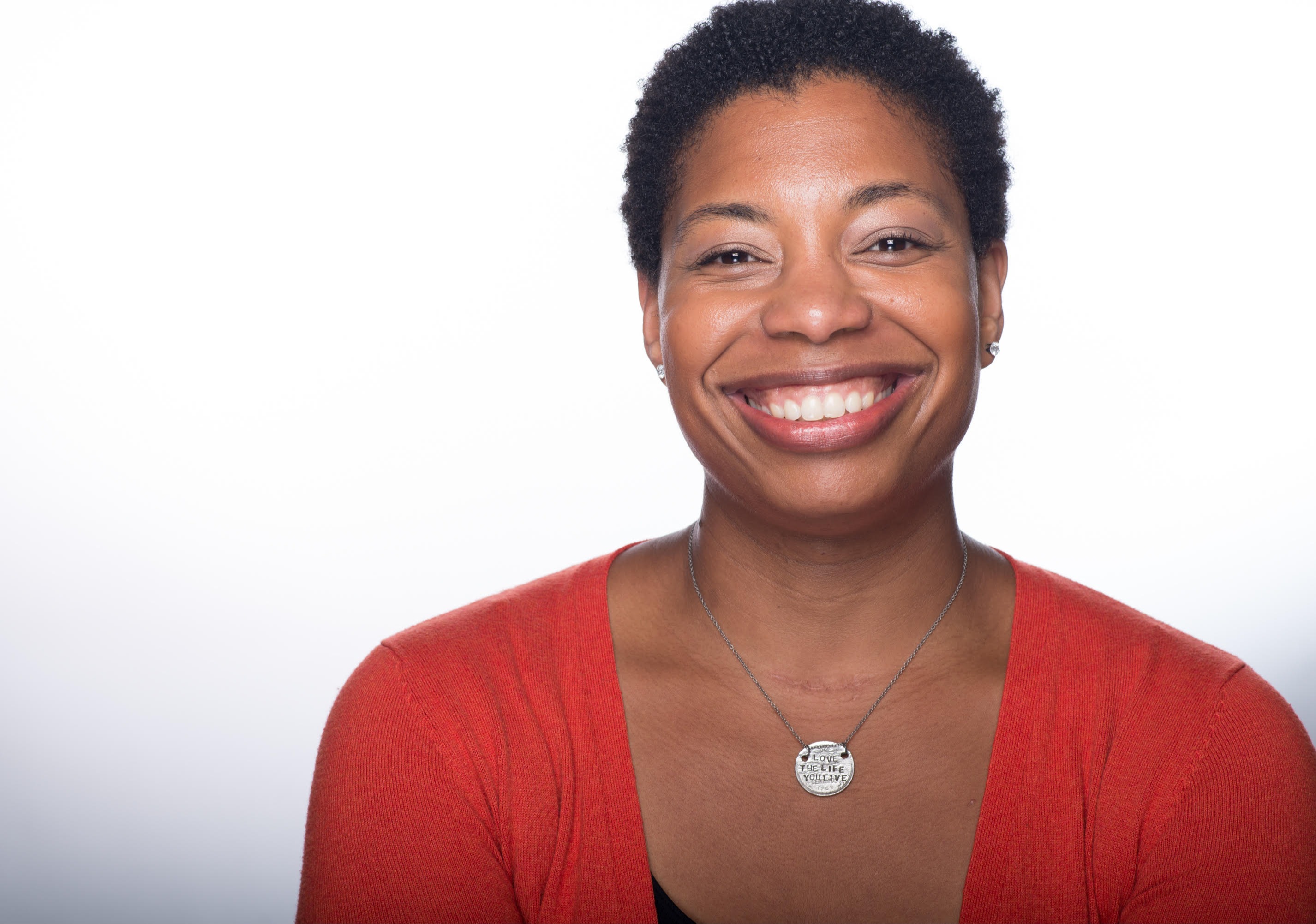 Reginé Gilbert, a Black woman with short curly hair, smiles at the camera while wearing an orange cardigan. 