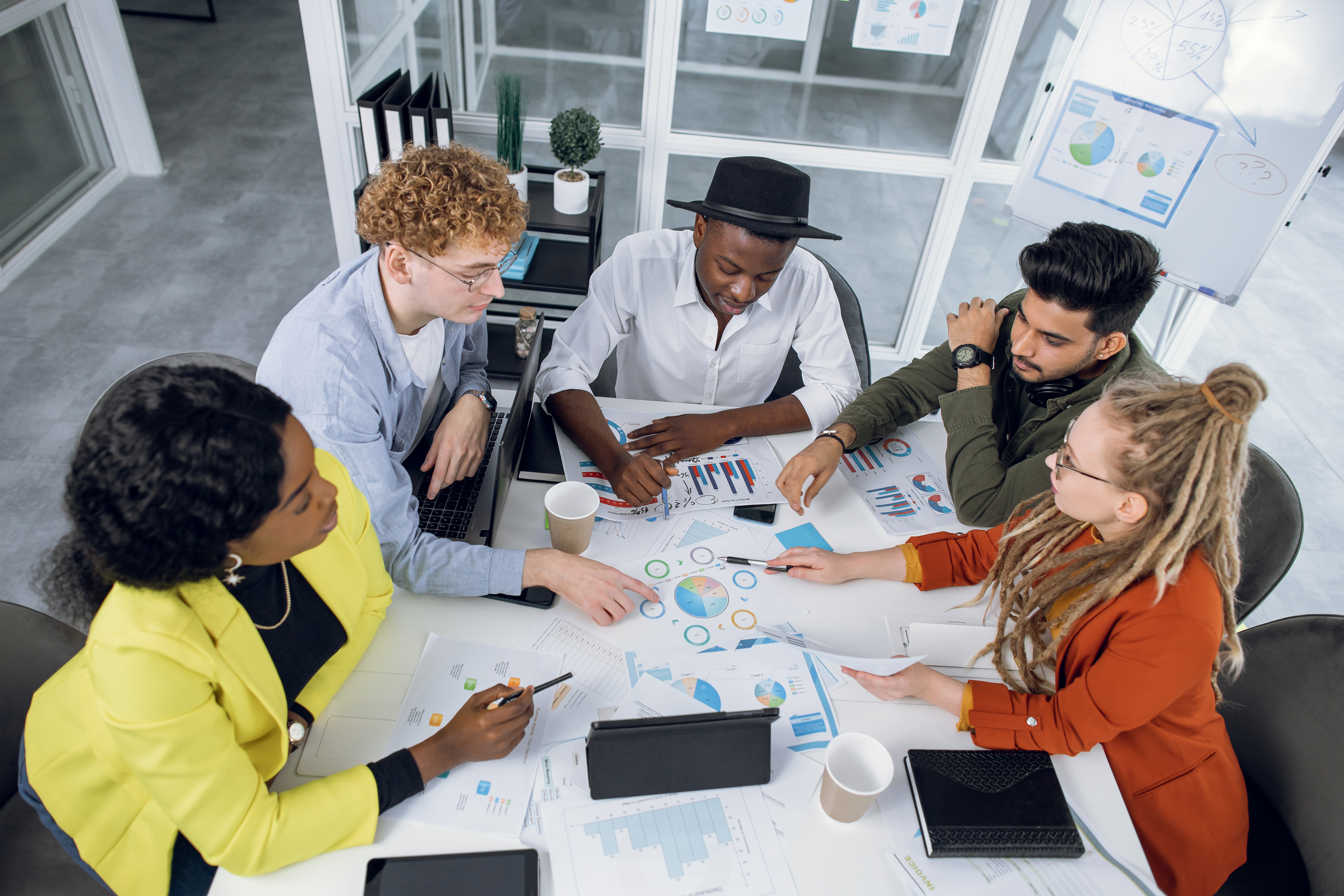 Team of young professionals sitting around table, pointing to charts on the table.