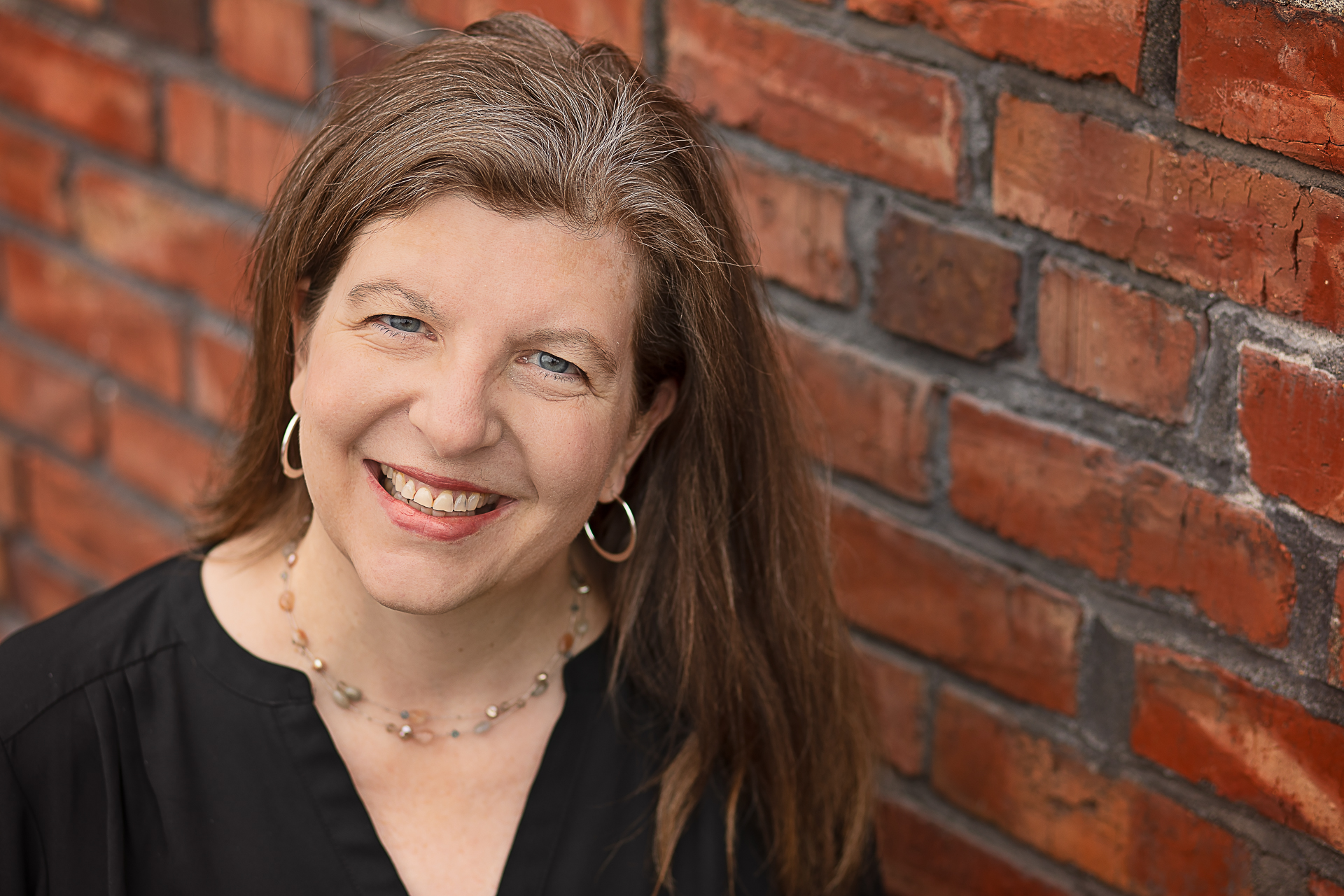 A headshot of Lynn, course instructor, standing in front of a brick wall.