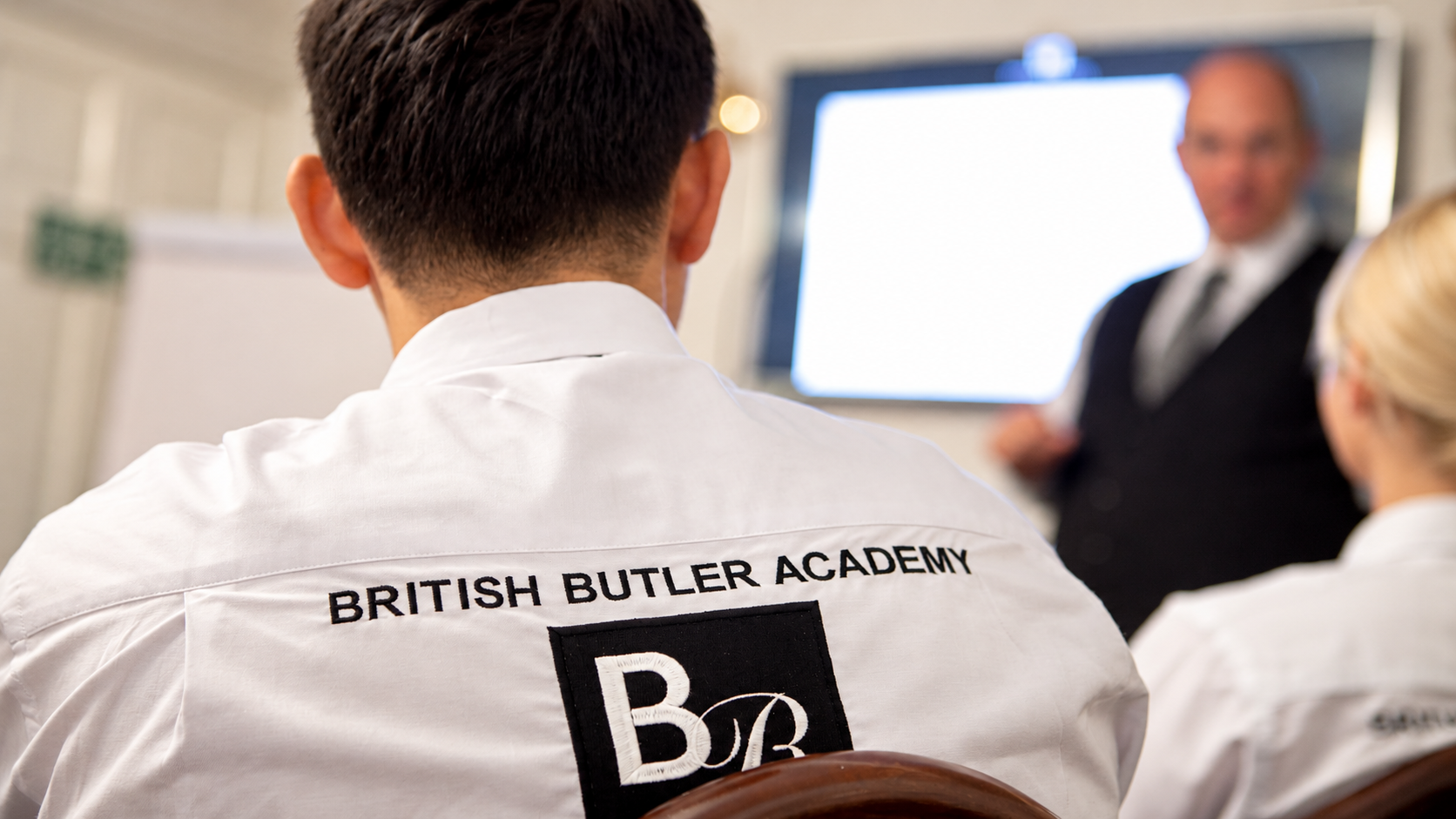 Students attending a British Butler Academy training session, with the Academy logo embroidered on a student’s shirt.