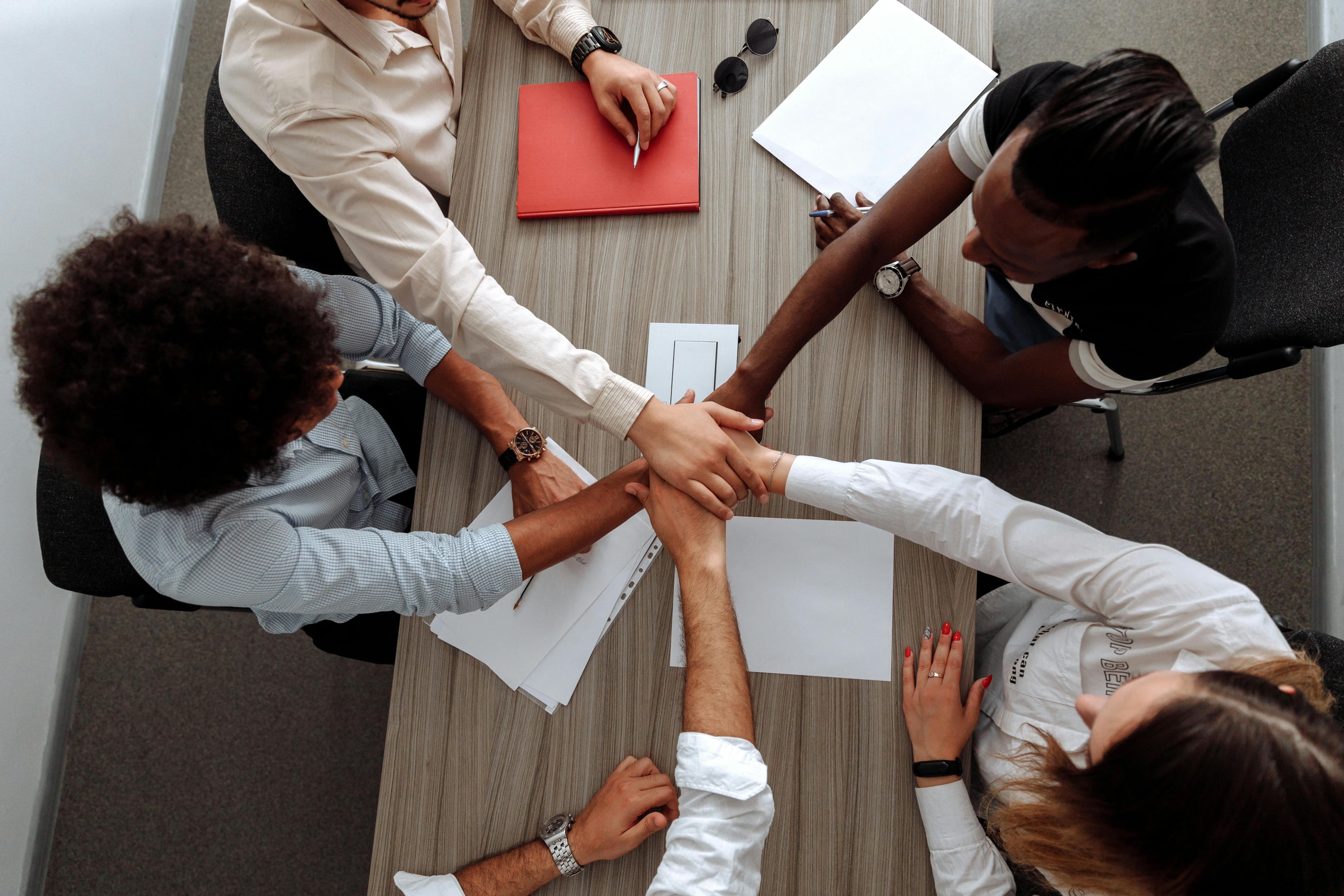 Collaborative group of people shown from above putting their hands together in a display of 'team work'