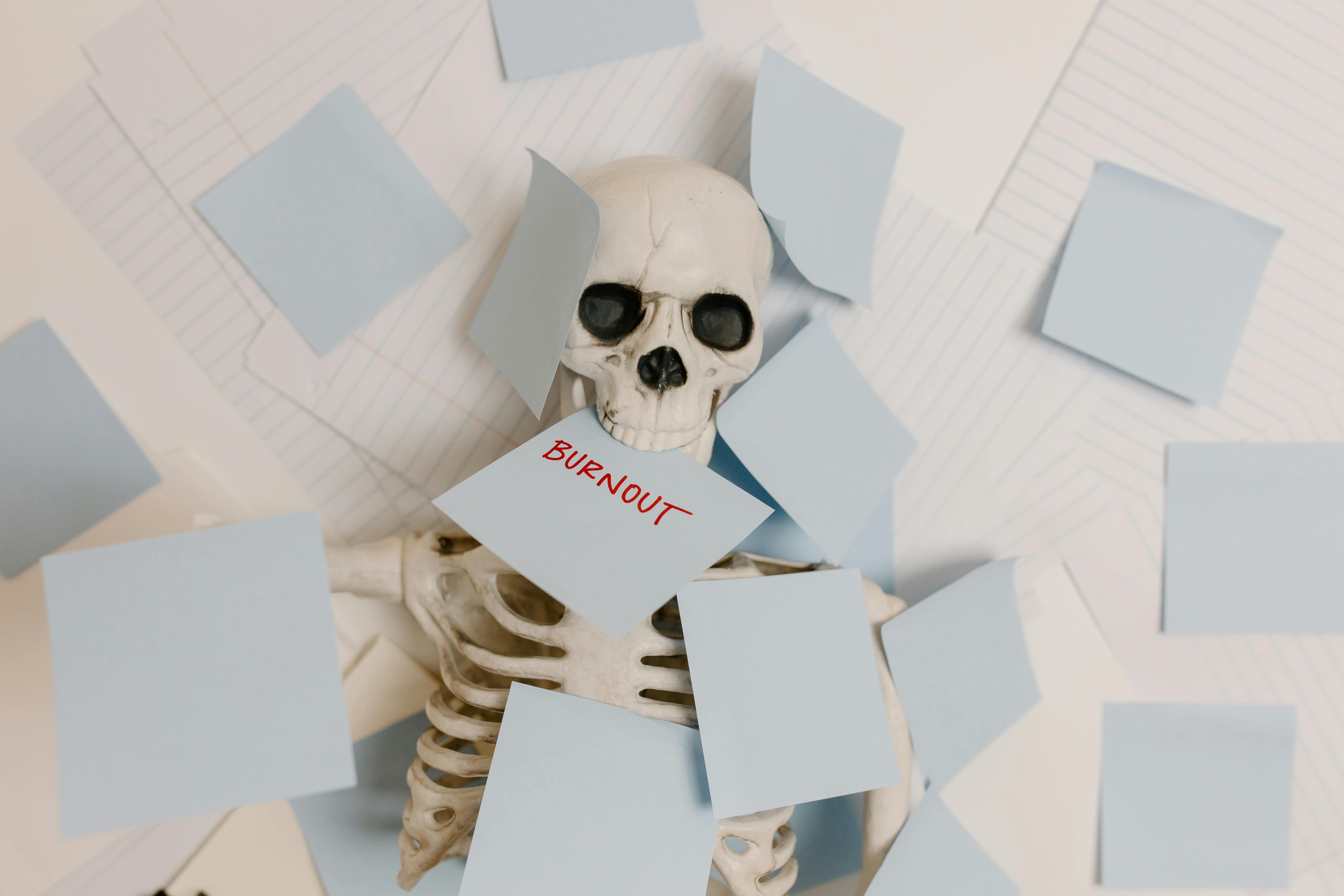 Skeleton surrounded by a mound of papers. A sticky note with the word 