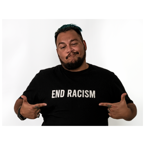 Jack Knoxville is a melenated transman with short dark hair and facial hair pointing to the words on his black shirt which read 