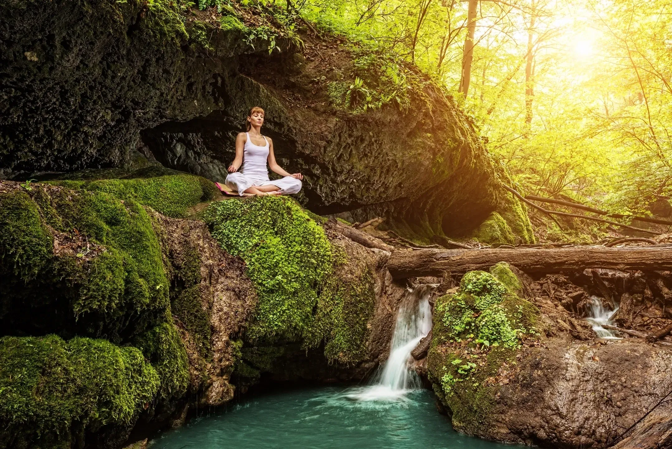 Image of a women meditating in nature, near small river.