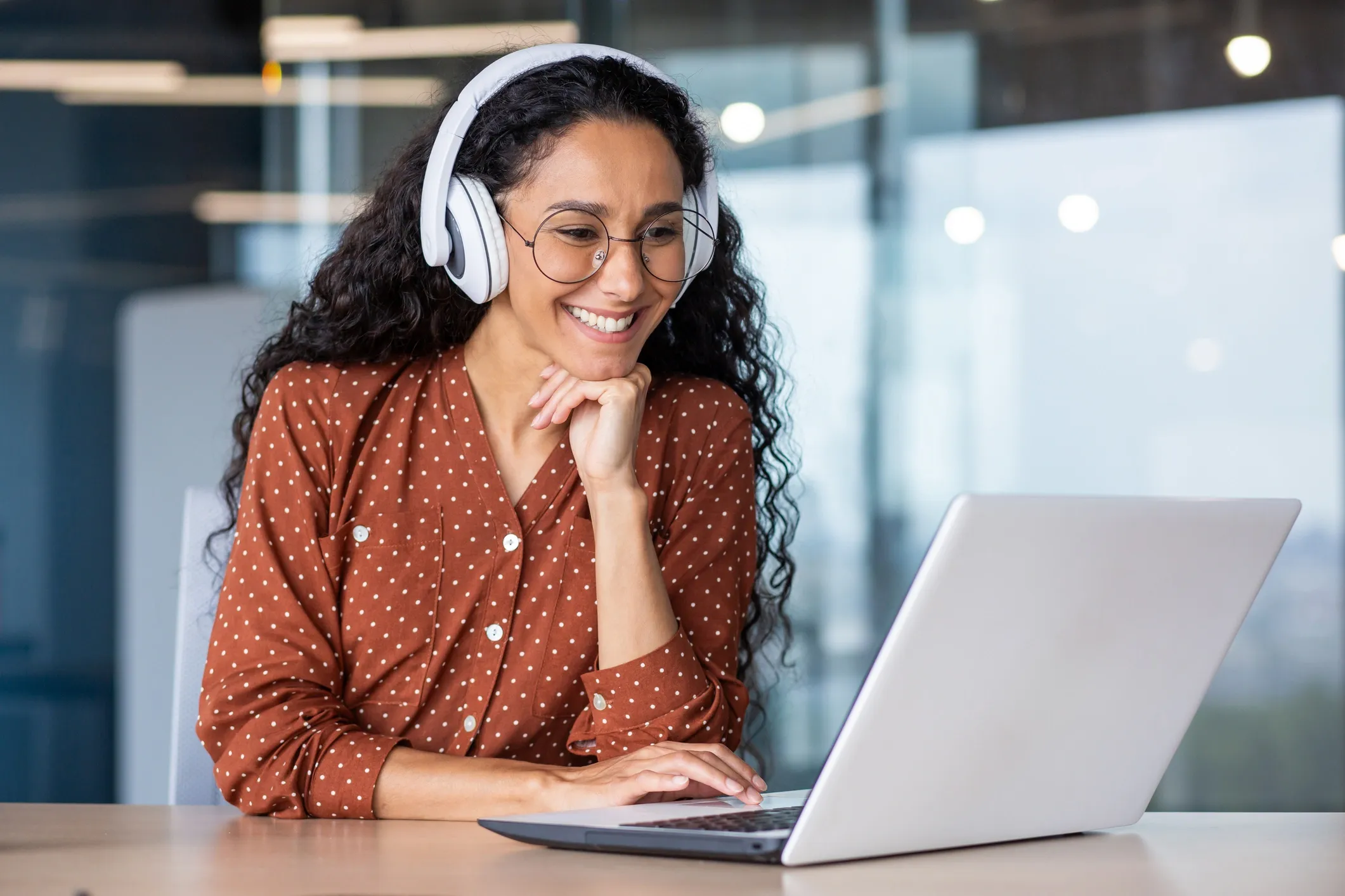 Image of a young women working on a laptop with headphones on. 