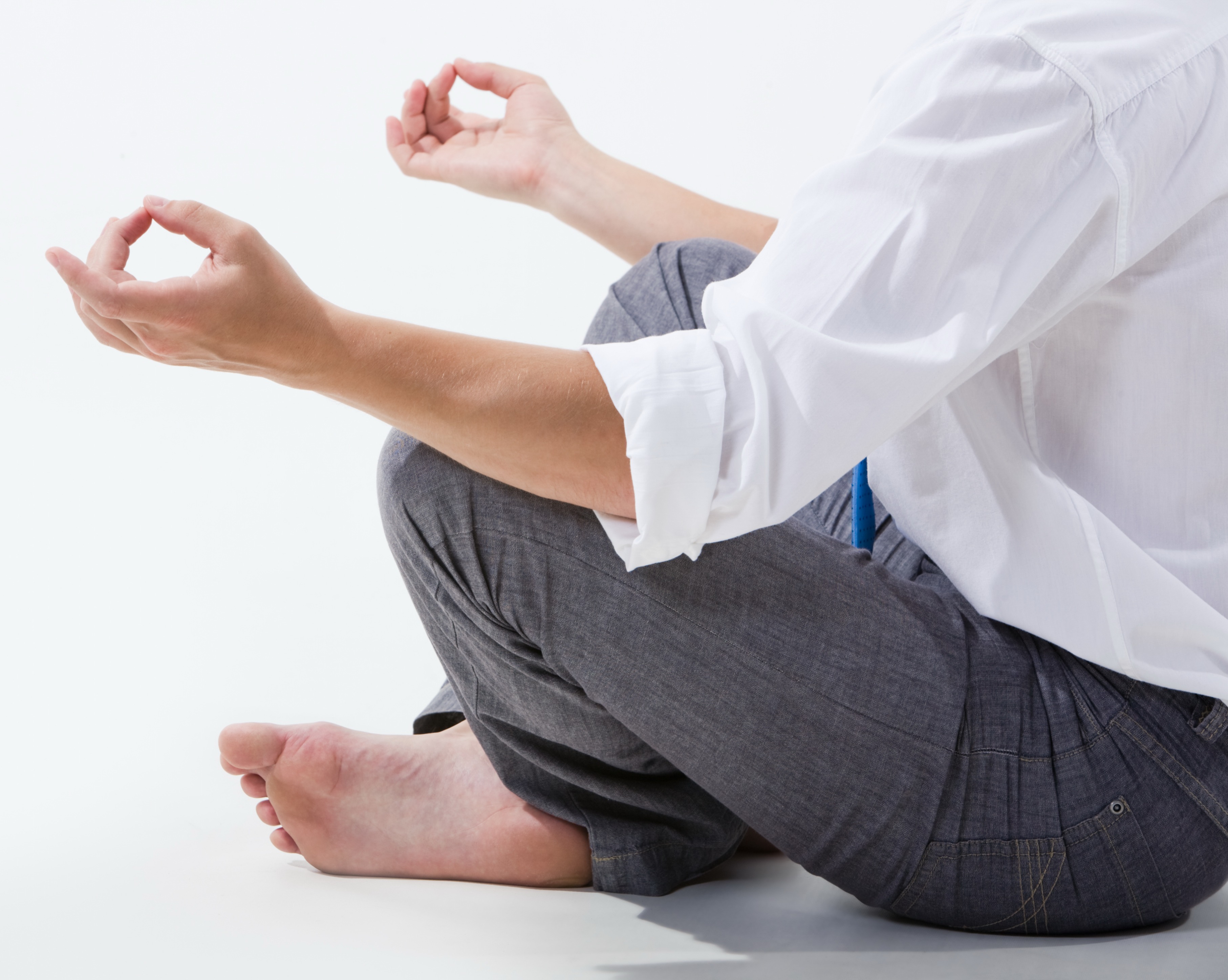 Stock photo depicting a person wearing business attire meditating in a crossed-legged position with forearms rested on knees and fingers positioned in a common meditation mudra