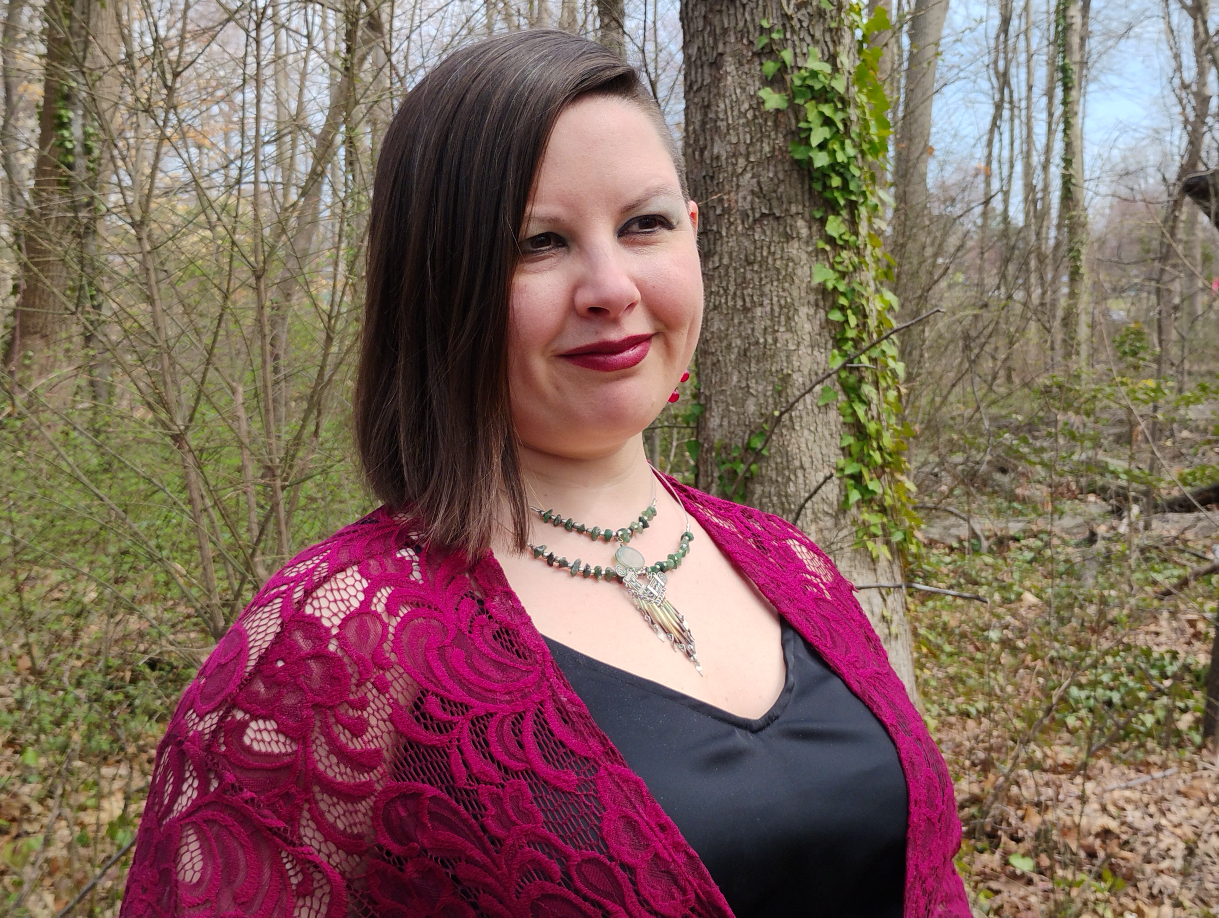 Photograph of Evylyn Rose, Empowerment Guide and Tarot Reader. She is smiling gently in an outdoor, wooded setting.