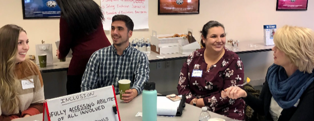 4 adults sitting at a table smiling and talking looking at a flip chart with INCLUSION at the top of the page.