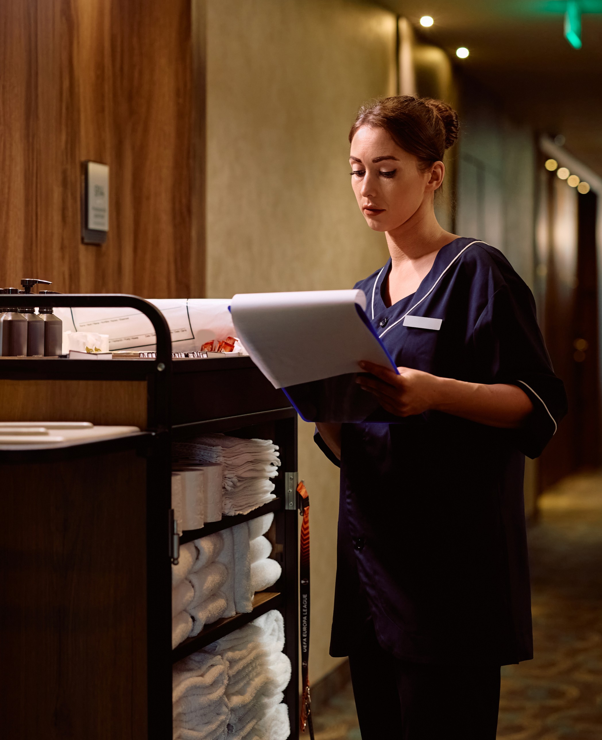 Hospitality professional performing room inspection with checklist in hotel corridor, demonstrating structured operational standards