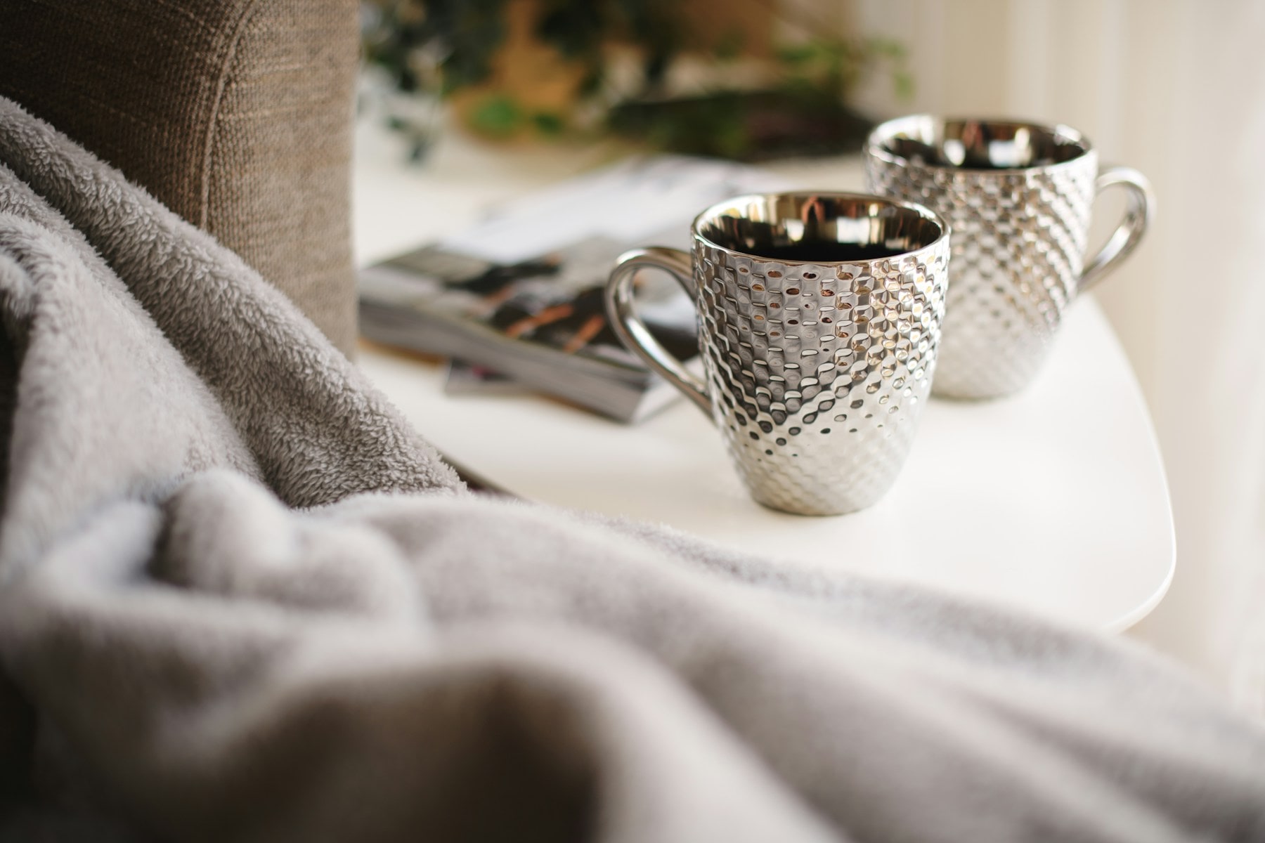 Two mugs on a small table beside a blanket, representing recovery and supportive connection.