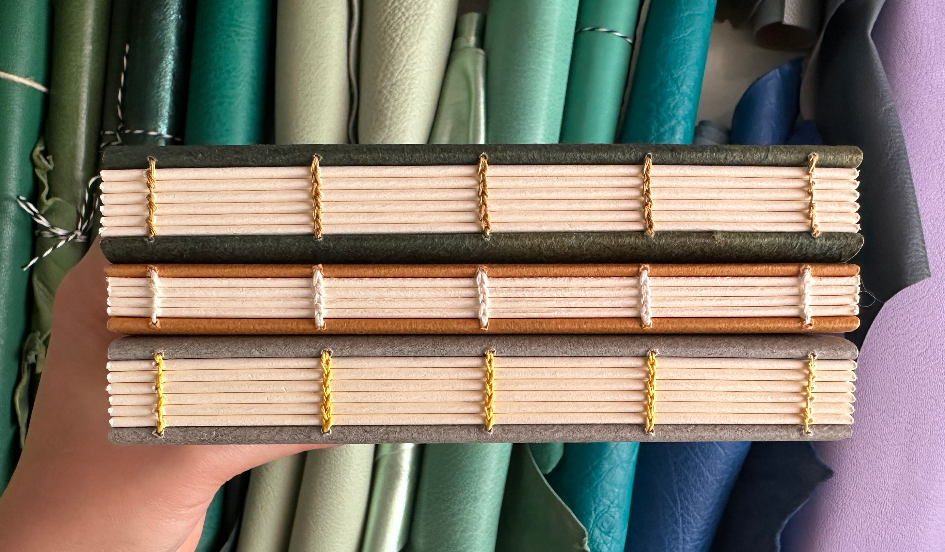 A hand holding three books with spines facing up to highlight exposed sewing.