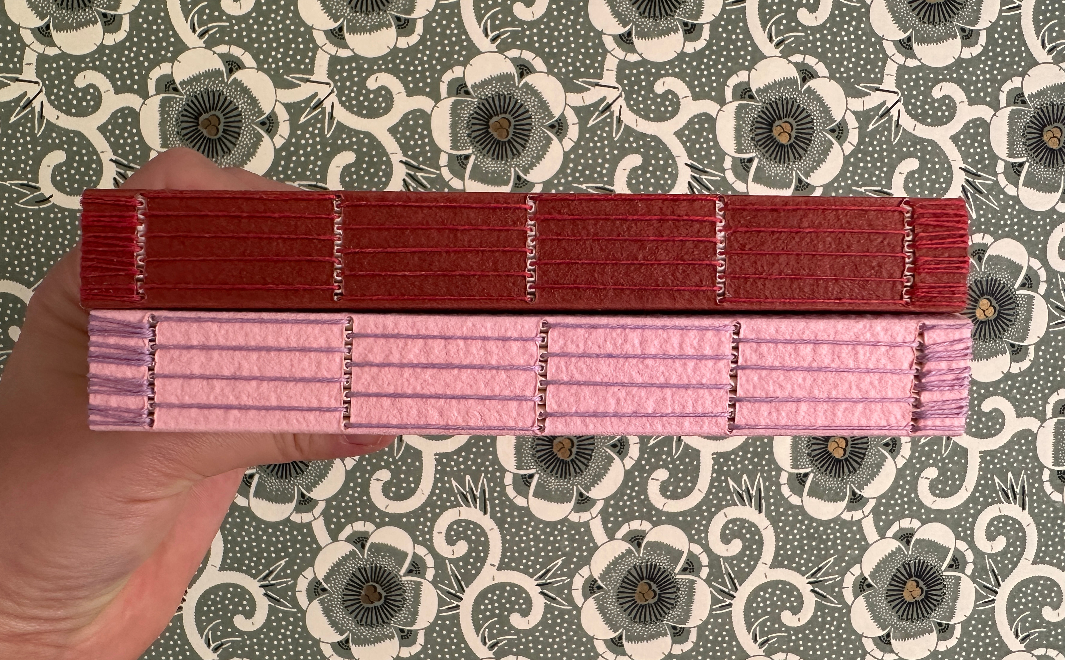 Hand holding two long stitch bindings with spine facing upward to show off sewing.