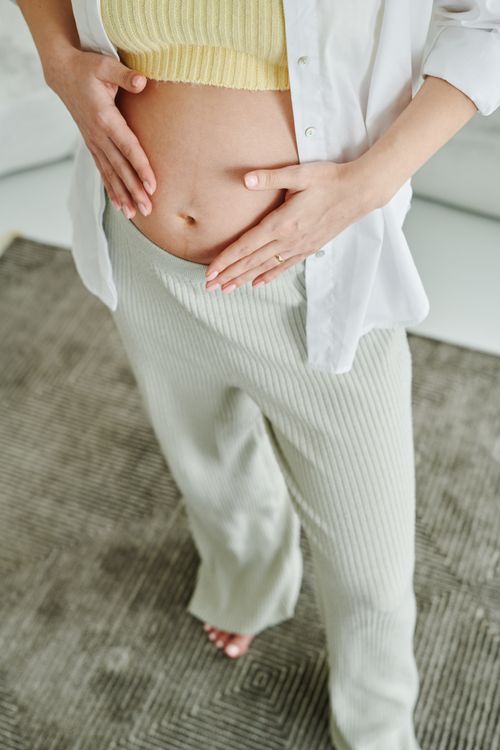 Pregnant person gently resting their hands on their belly.