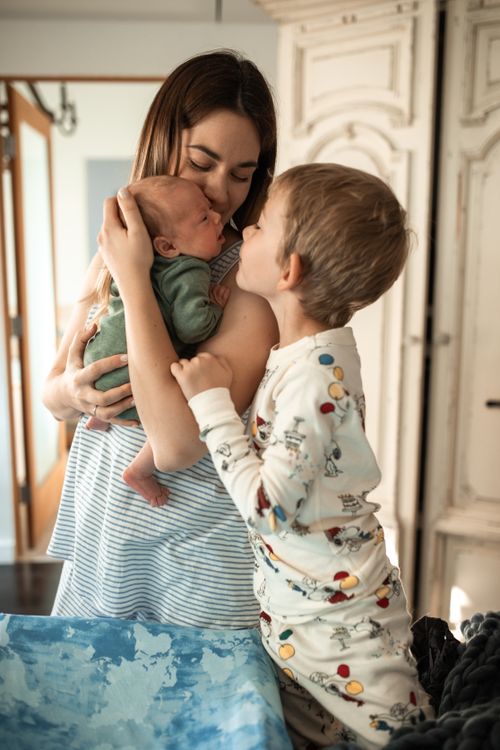 A mother holding her newborn while her older child embraces her.