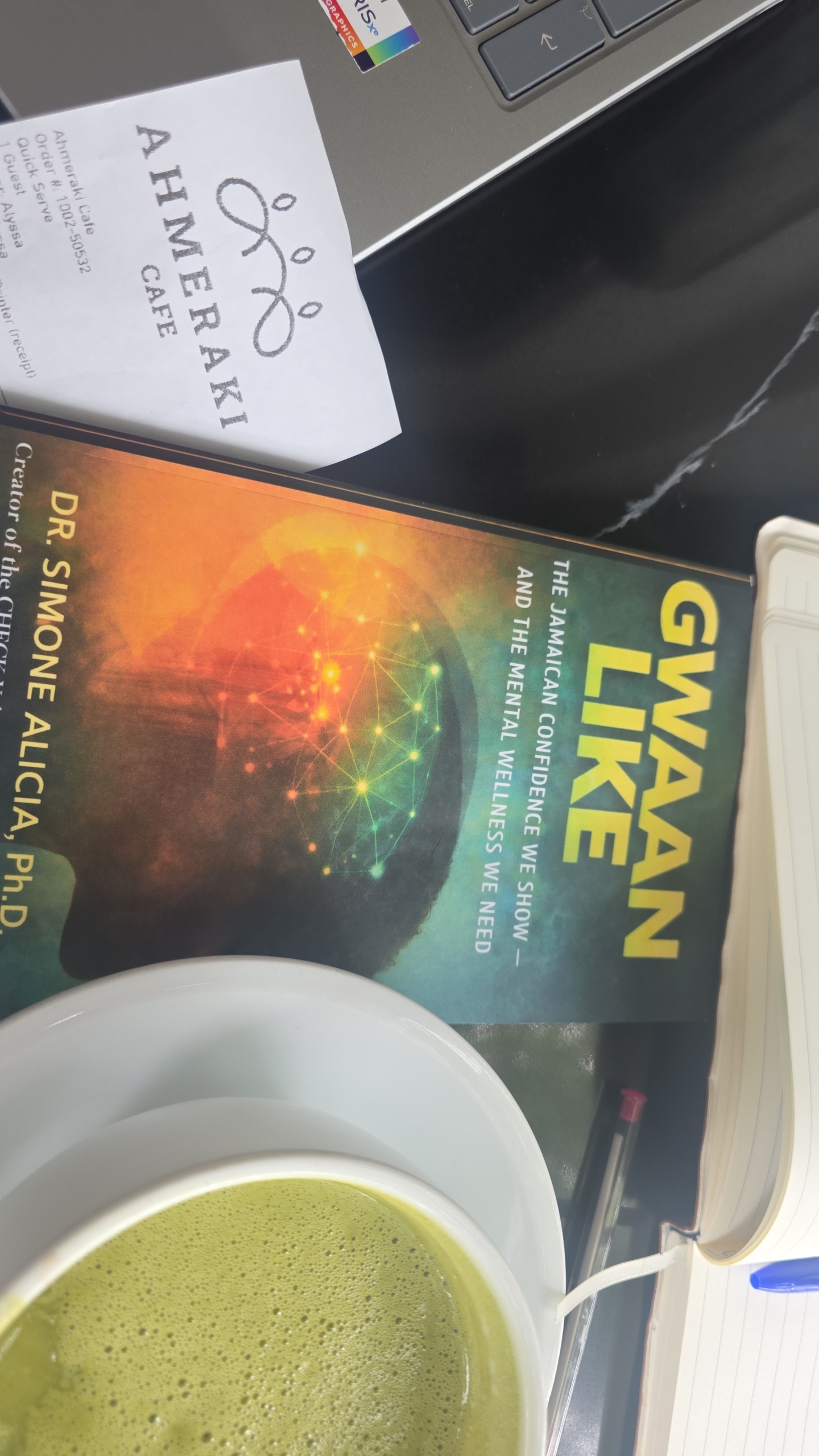 GWAAN LIKE book beside a journal and drink at Ahmeraki Cafe in Jamaica
