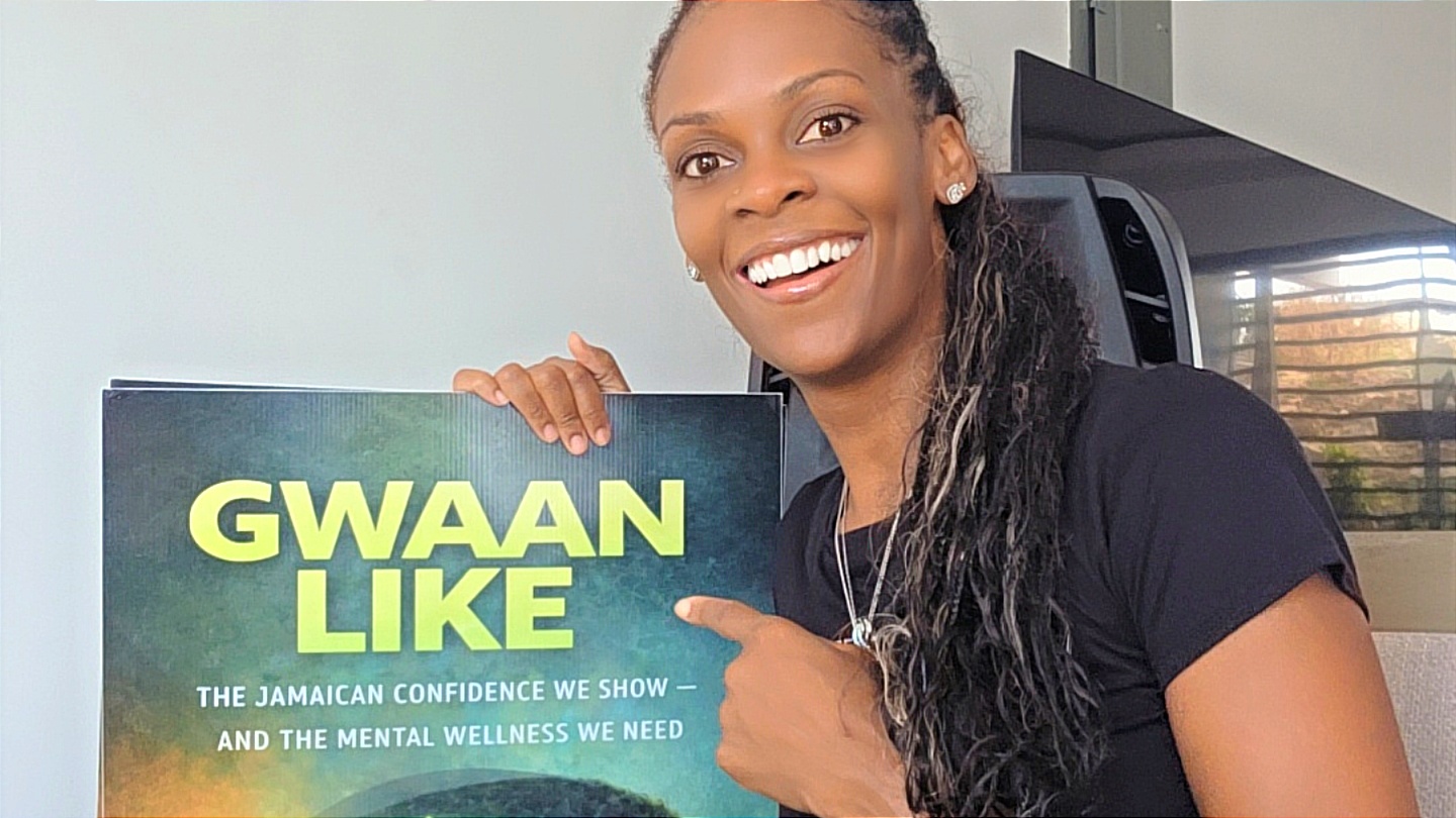 Dr. Simone Alicia holding the GWAAN LIKE poster featuring the book’s Jamaican mental wellness message