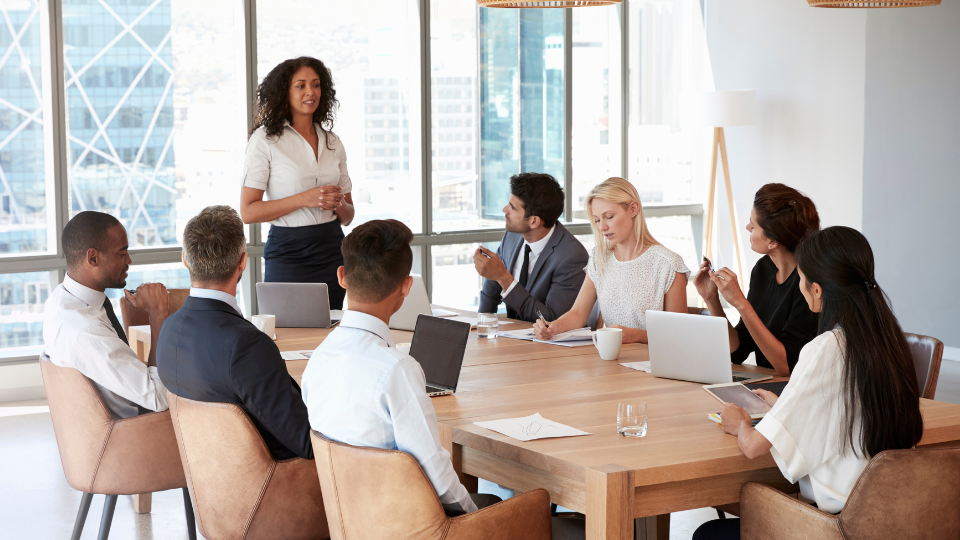 Team meeting with a woman stood at the front of a boardroom table.