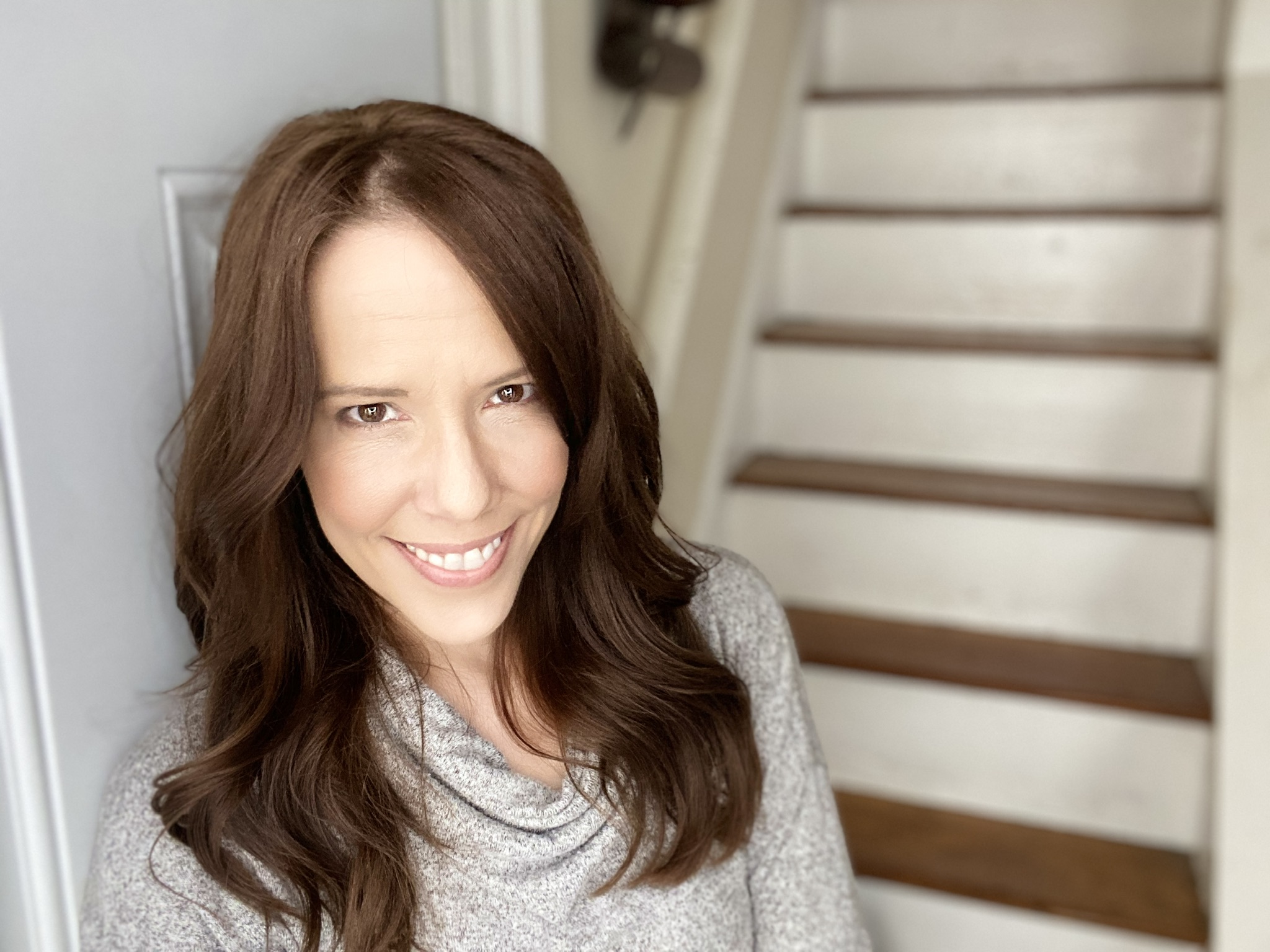Image of a dark haired woman - Lori Petro - sitting on painted white wooden steps.