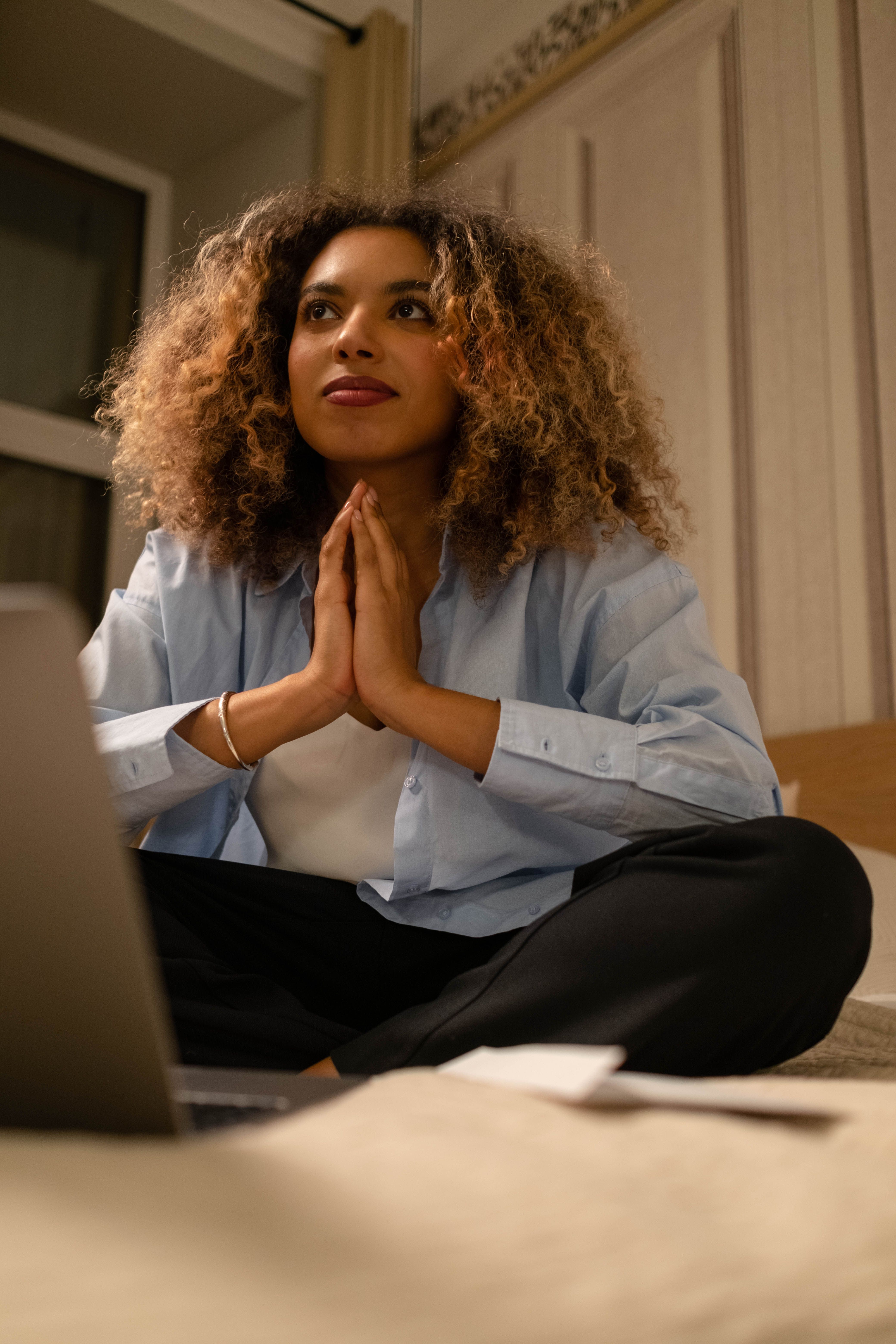 Woman with prayer hands sitting on bed surrounded by work
