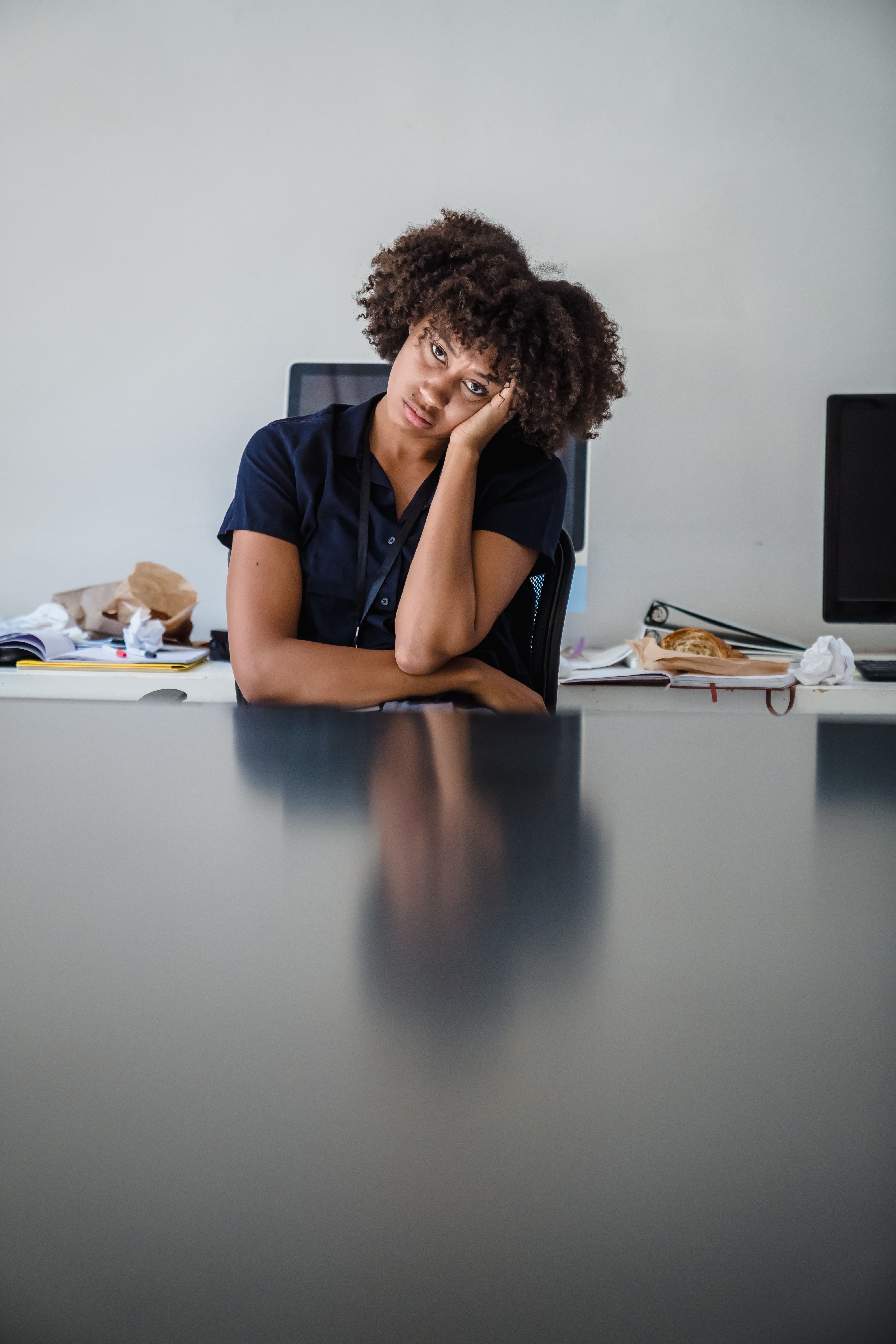 Tired seeming woman with head in hands in a messy office