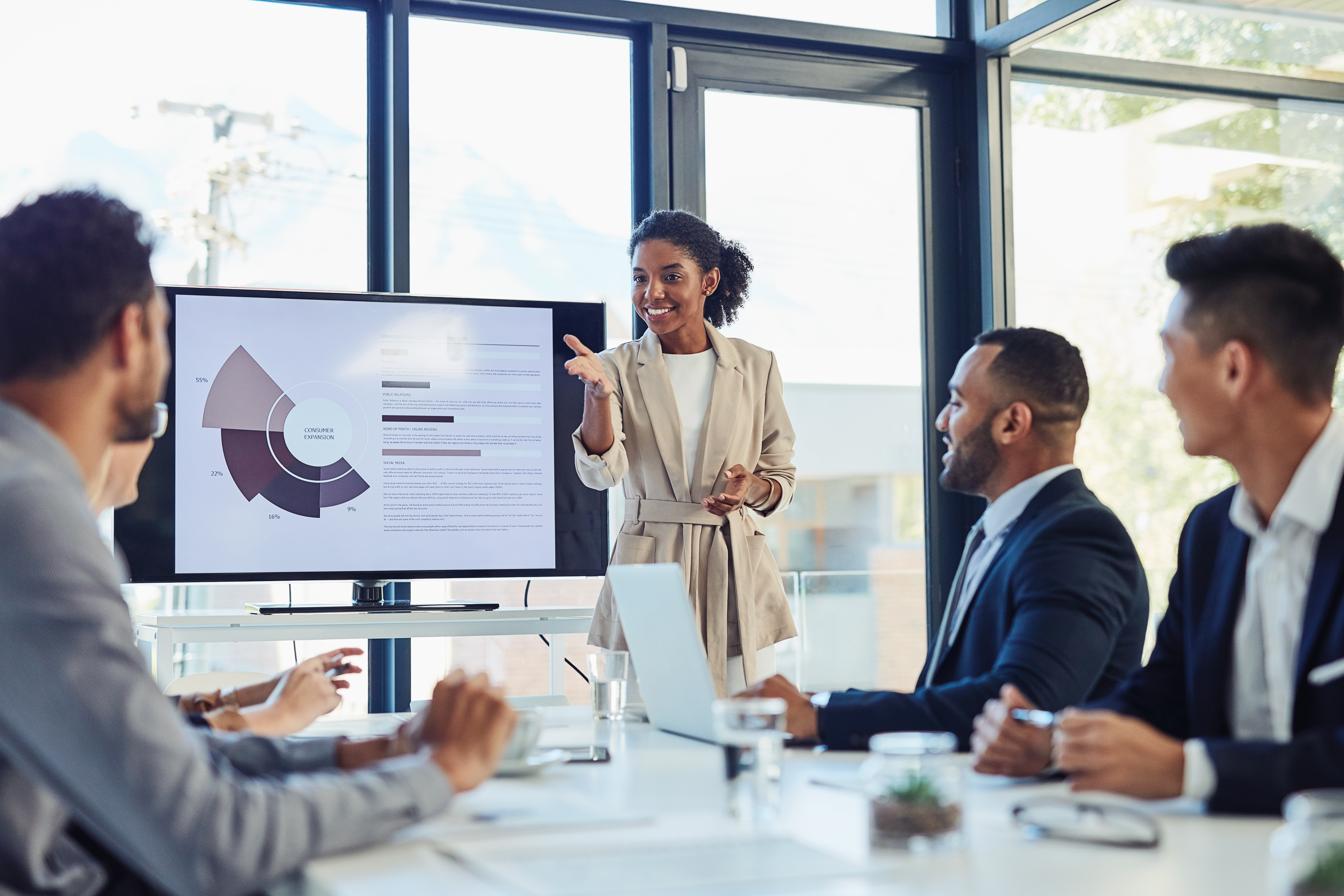 young black data analyst presenting to a team of men with a computer monitor with statistical data. She is gesturing to an engineer inviting his perspective.