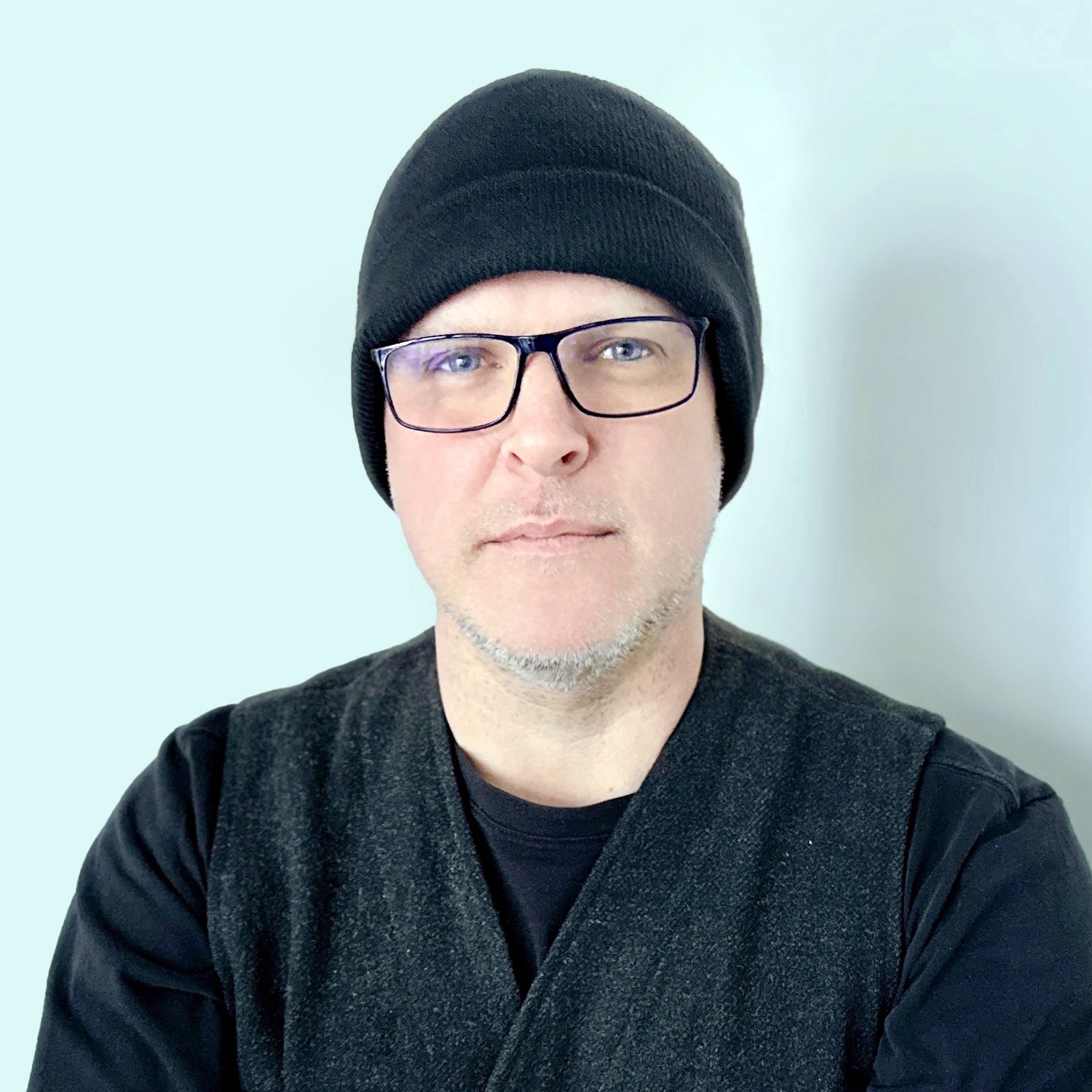 Headshot of Lee Herrin wearing a black vest, black shirt, glasses, and a black toque.