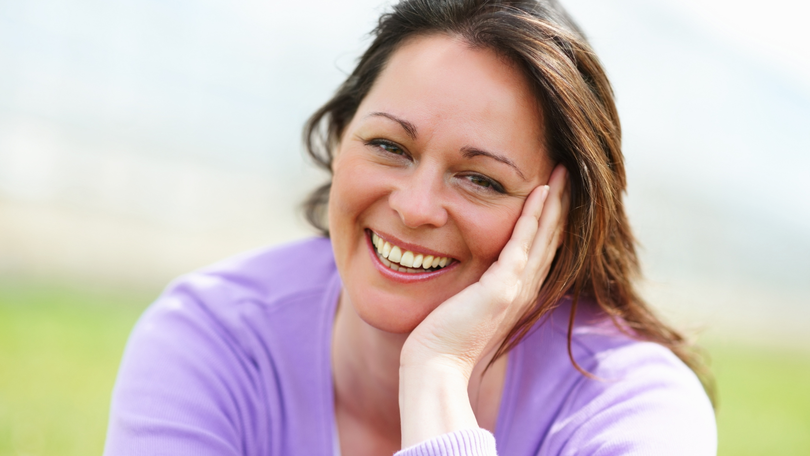 Portrait of a smiling woman resting her head on her hand outdoors.