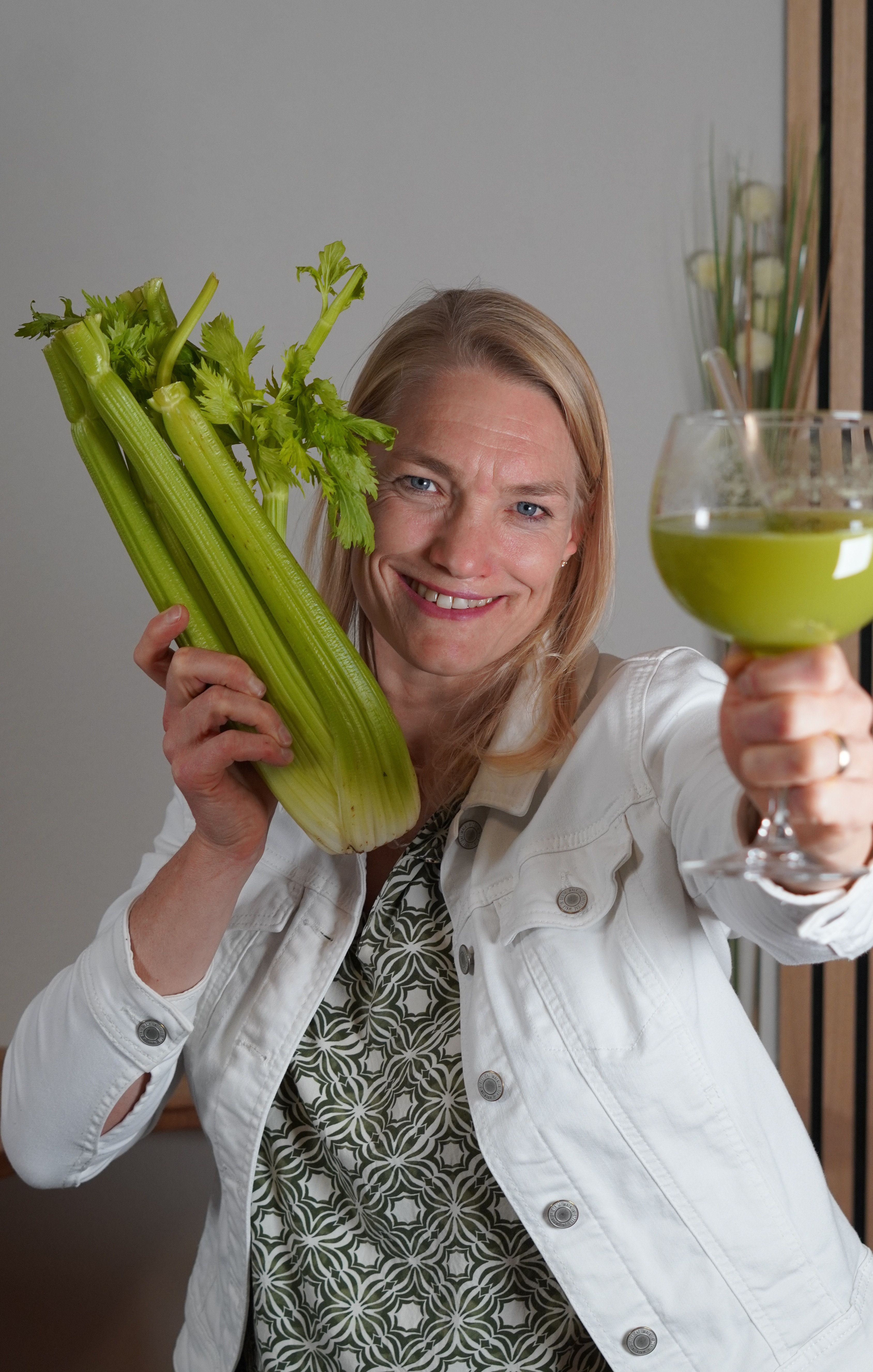 Person (Birgit Trauner) mit Glas Selleriesaft und Bund Sellerie in der Hand