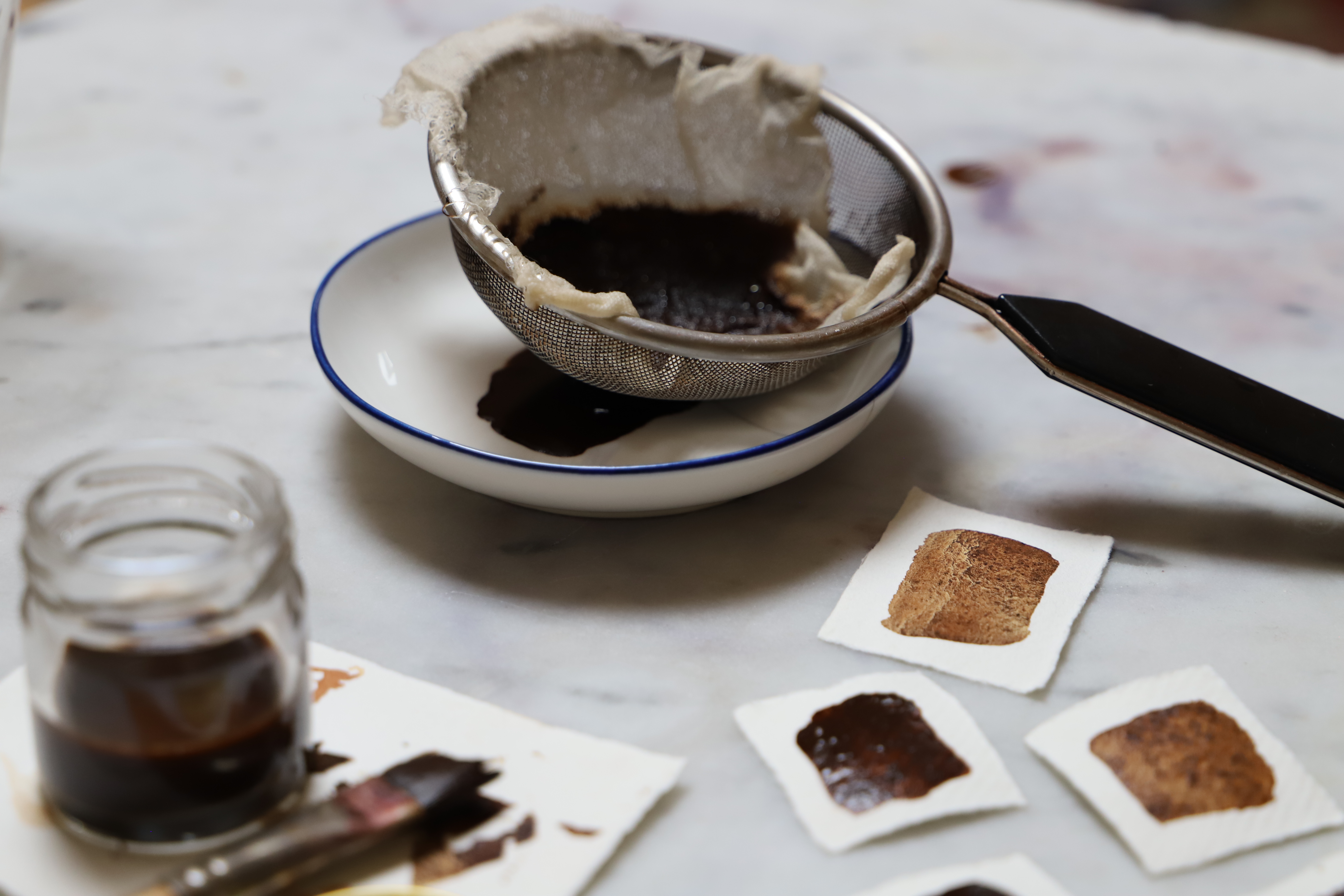 Botanical paint strained onto saucer with swatches of watercolour paint on handmade cotton paper