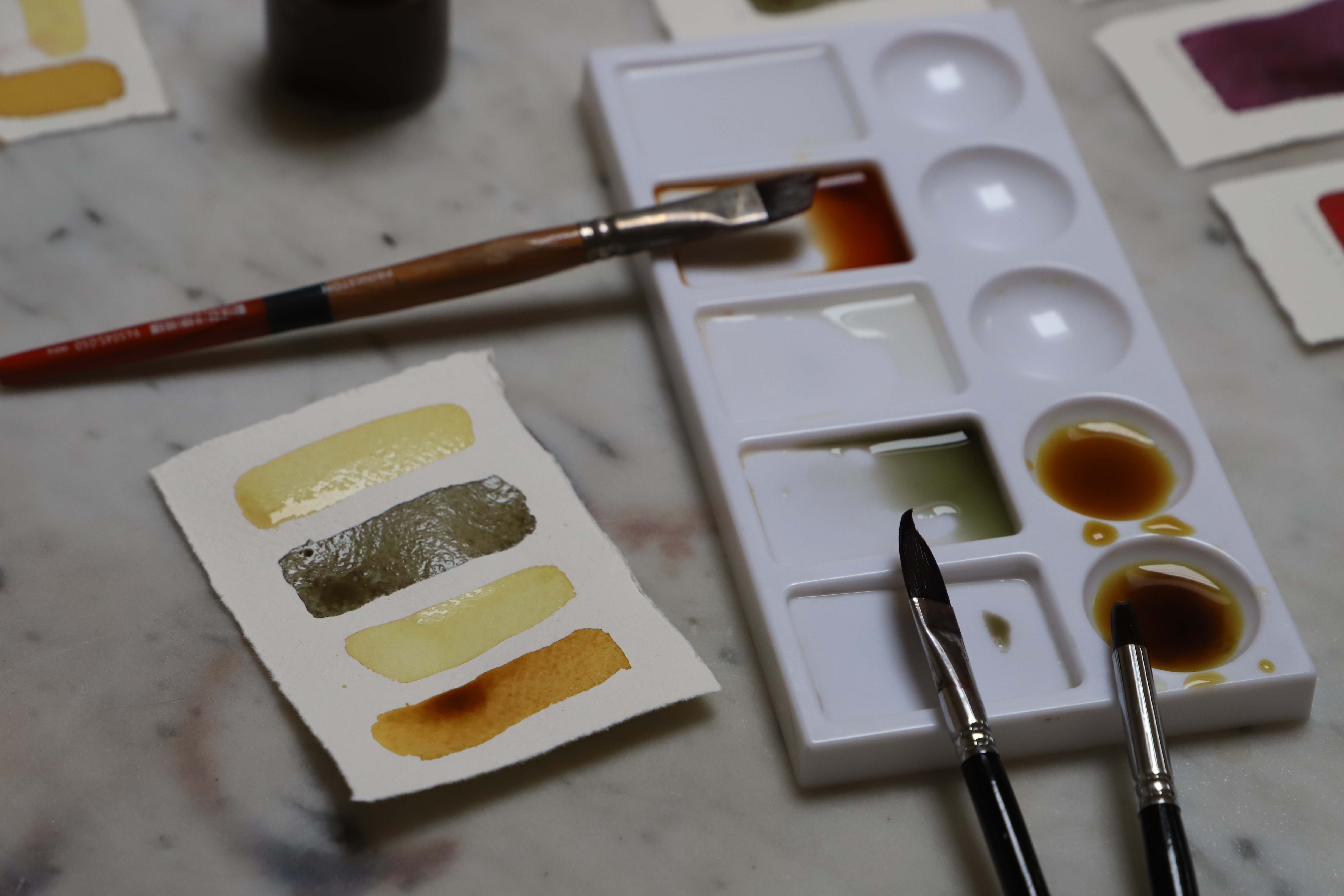 paper swatch with three naturally made botanical paints painted on handmade cotton paper next to closeup of paintbrush