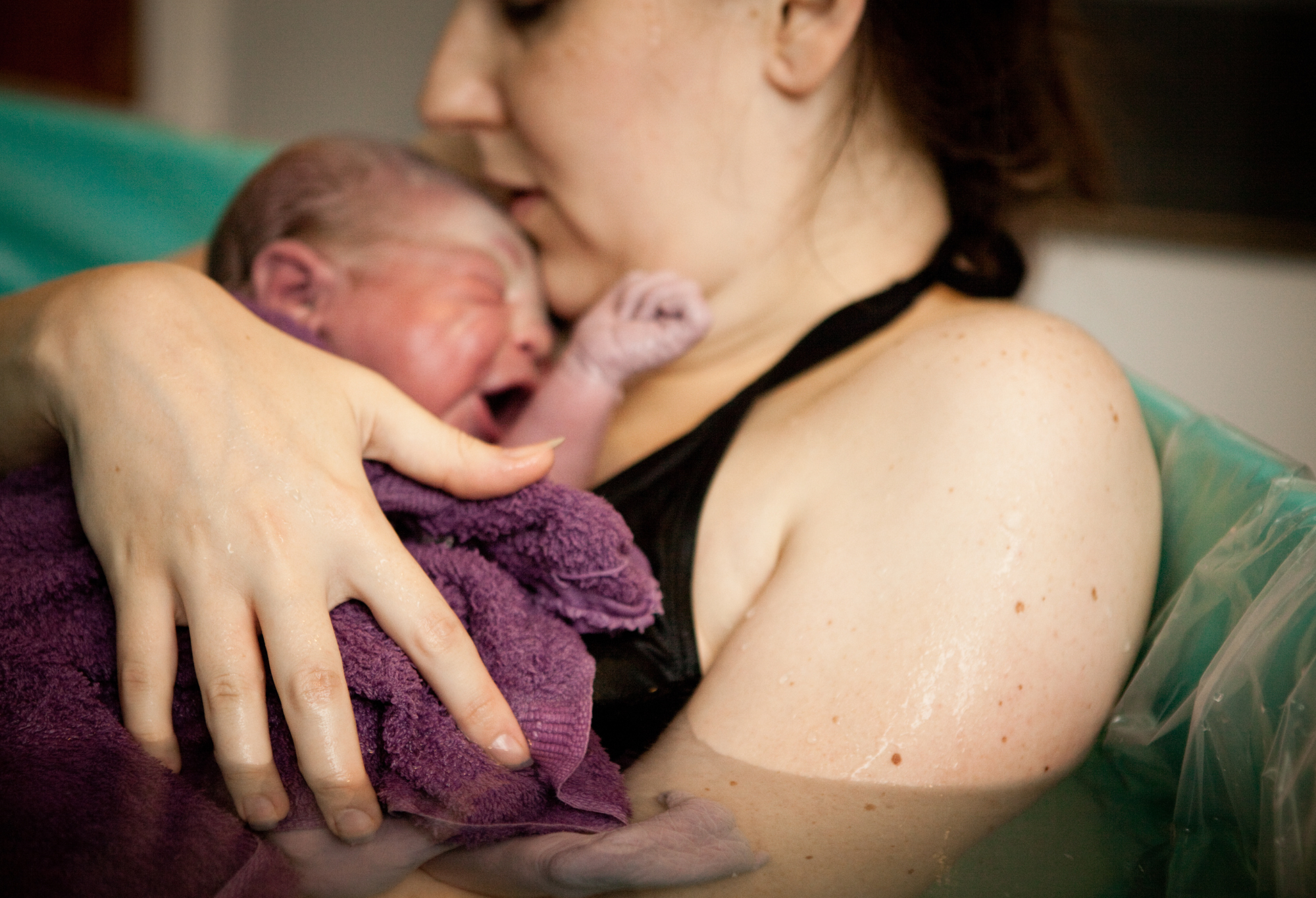 woman in birthing tub with baby in arms