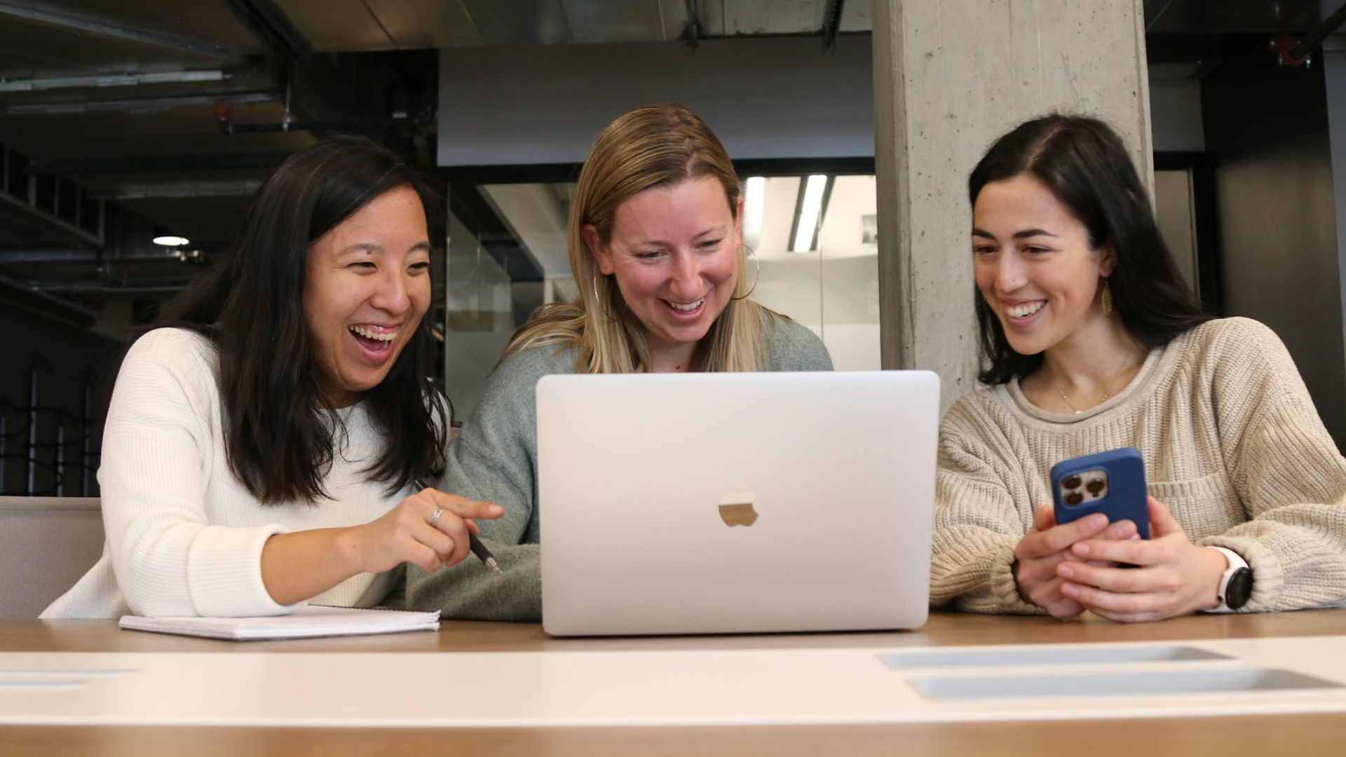 The Purpose Collective team members smiling, looking at computer screen.