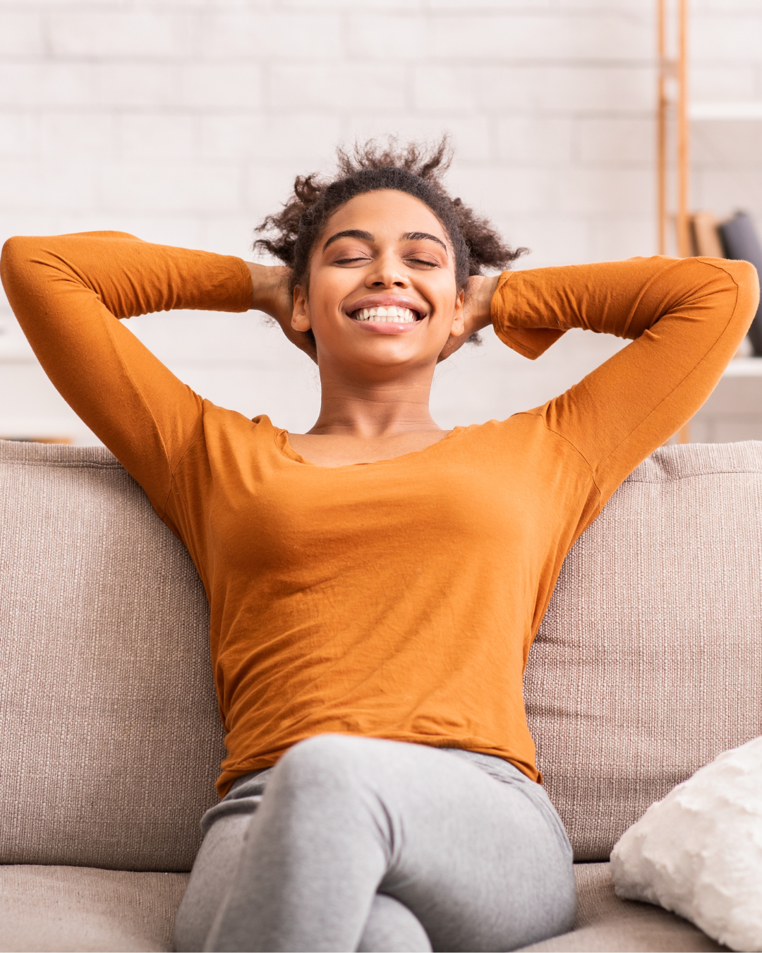 Woman sitting and leaning back, smiling and relaxing with hand behind head.