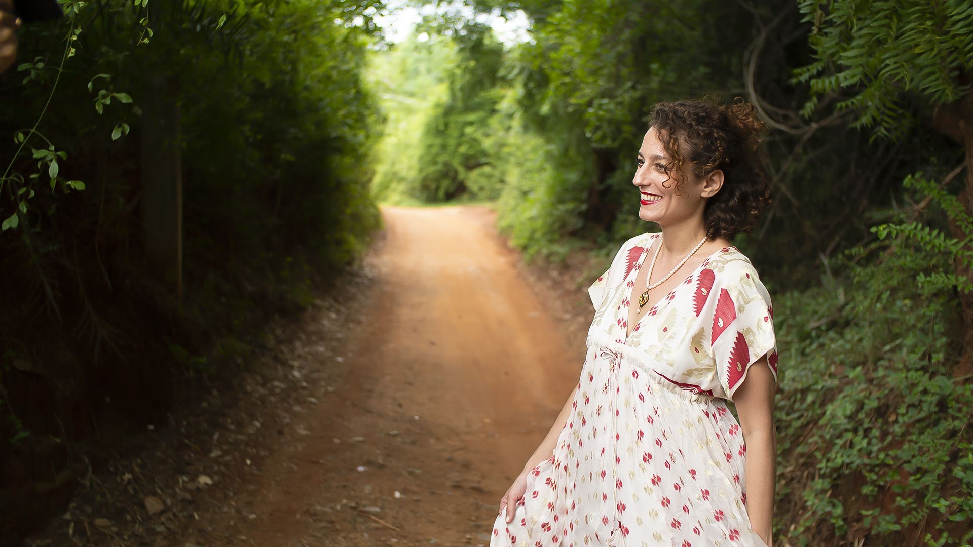 Alia marchant sur un chemin bordé de nature, souriante, symbole de transmission et d’ancrage dans la formation Yoga de la Femme.