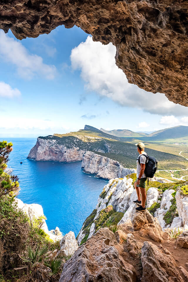 A man standing on a rocky cliff while staring off into horizon.