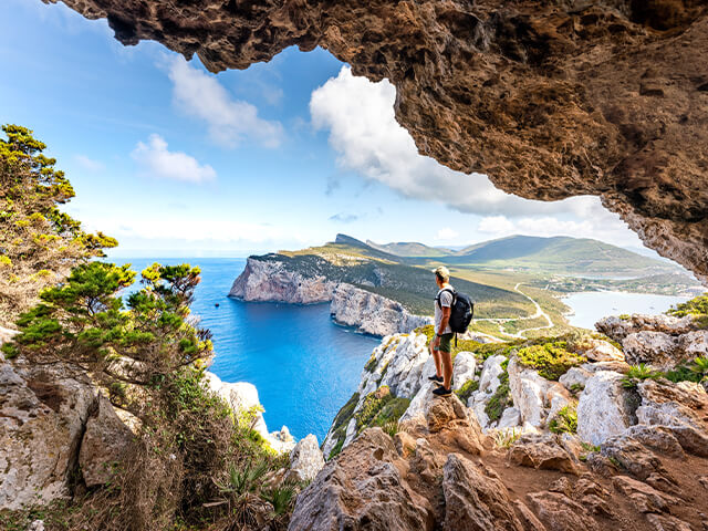 A man standing on a rocky cliff while staring off into horizon.