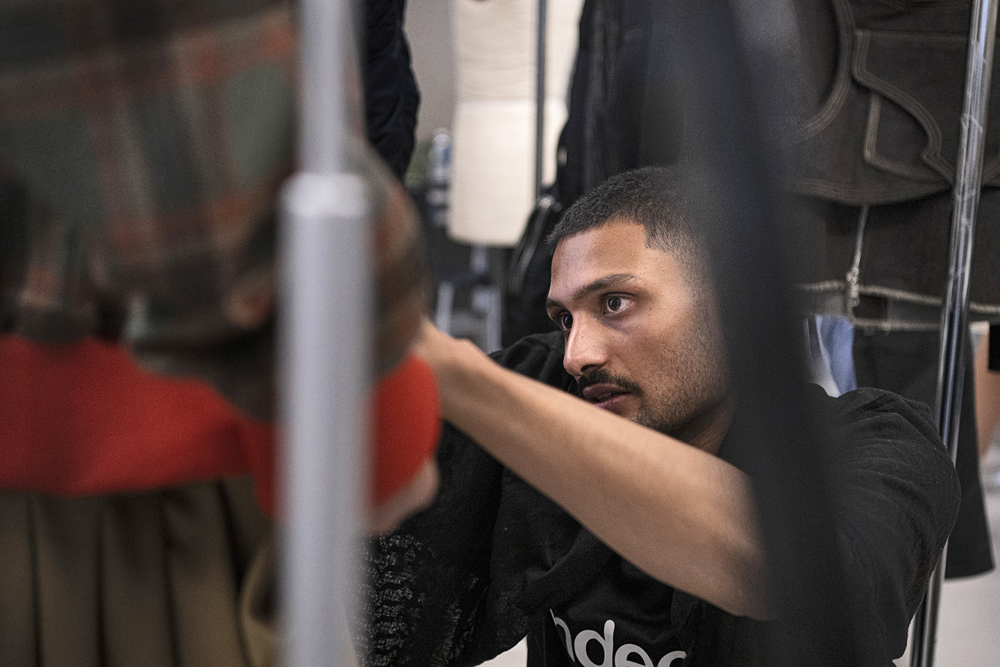 Closeup looking through garments hanging on a rack at a student diligently adjusting a garment on a fit model
