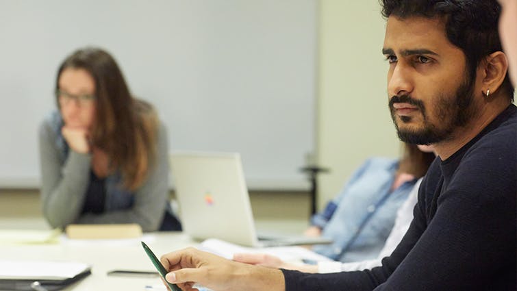 A serious student sits in a classroom with other students.
